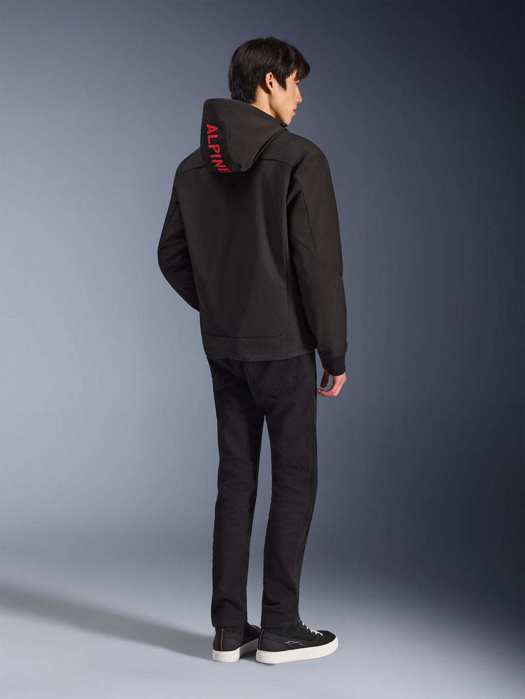 Alpinestars Radium Tech Hoodie, sort med rød Alpinestars-branding på hætten, set bagfra på en mandlig model, båret med sorte bukser og sneakers, teknisk urbant køreudstyr