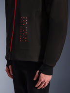 Alpinestars Radium Tech Hoodie, urban motorcykeljakke, sort og klar rød, nærbillede af frontgrafik med lodret rød tekst 'ALPINESTARS ONE GOAL ONE VISION', rød lynlås og ribbet manchet med tommelfingerhul.