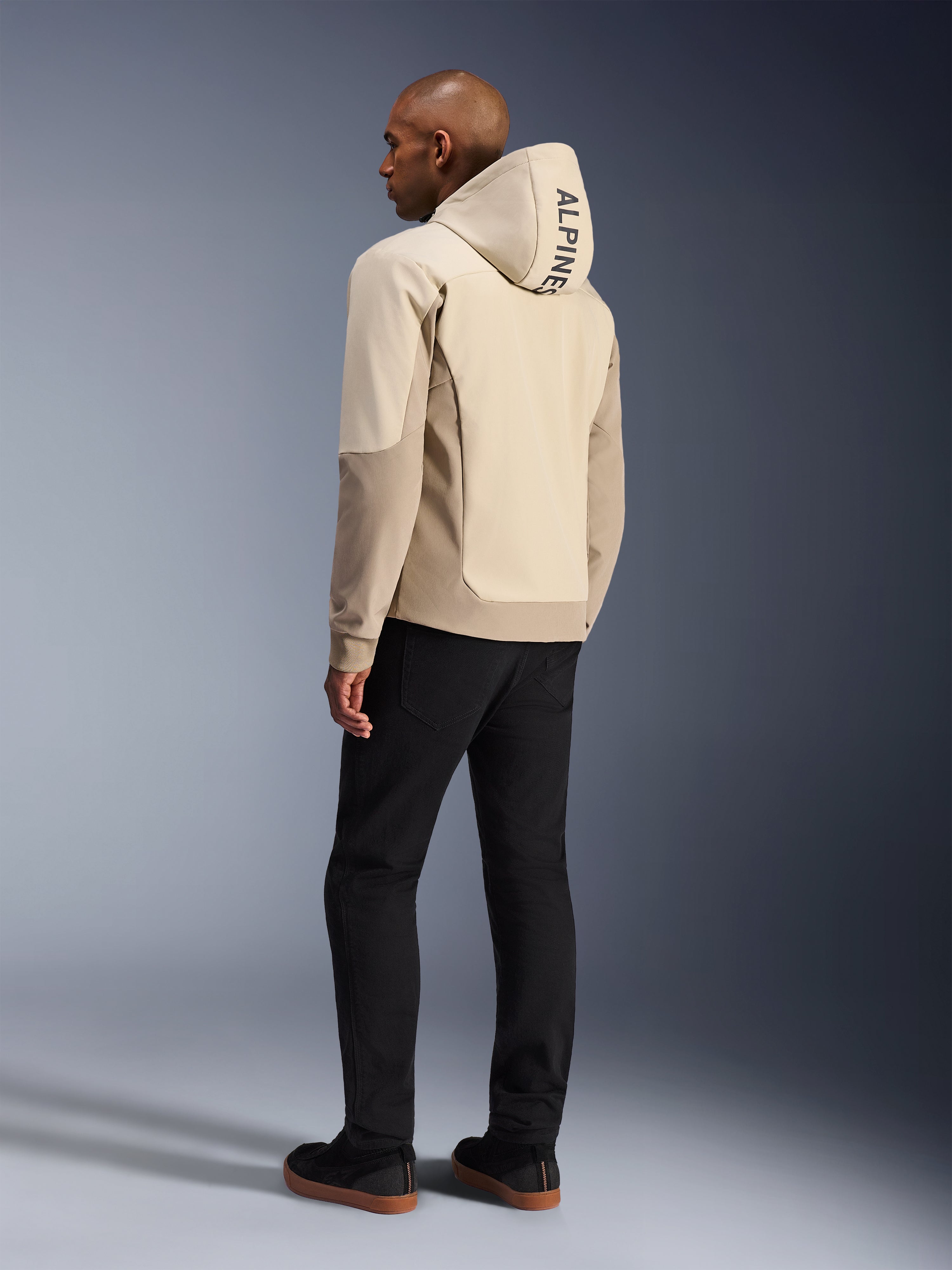Alpinestars Radium Tech Hoodie i Mastic Aluminum, urban motorcykeljakke, set bagfra på model med hætten oppe, lodret ALPINESTARS-branding på hætten, kombineret med sorte bukser, moderne tekstilkonstruktion til beskyttelse ved bykørsel