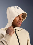 Alpinestars Radium Tech Hoodie i Mastic Aluminum, nærbillede af en mand med hætten oppe, med Alpinestars-branding på toppen, urban motorcykeljakke med teknisk vindtæt skal, moderne streetwear-æstetik til bykørsel
