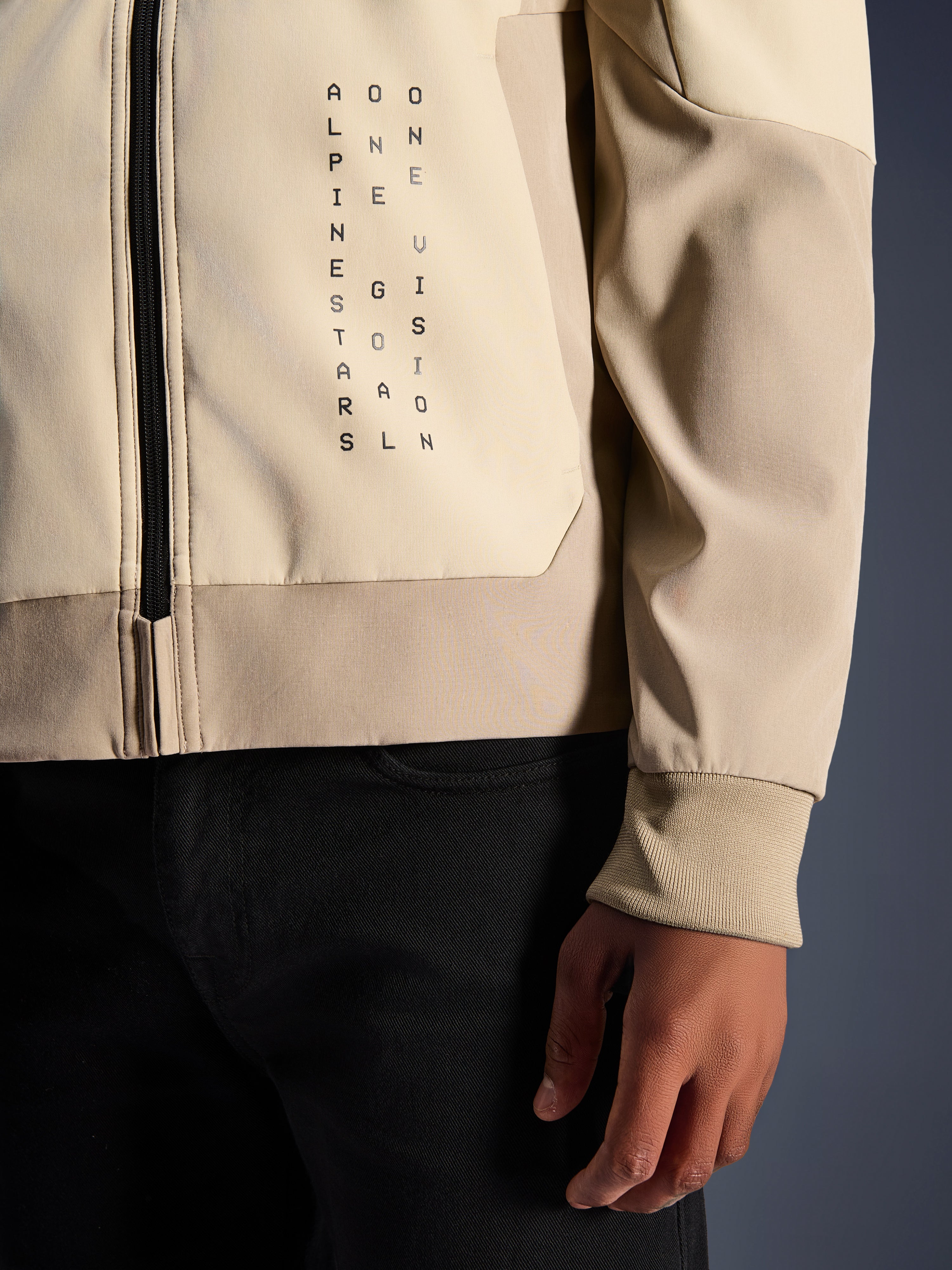 Alpinestars Radium Tech Hoodie i Mastic Aluminum, nærbillede af bryst og ærme, lodret sort tekstbranding 'Alpinestars One Goal One Vision', ribstrikket stretchmanchet og lynlåsdetalje, urban motorcykel tekstiljakke.