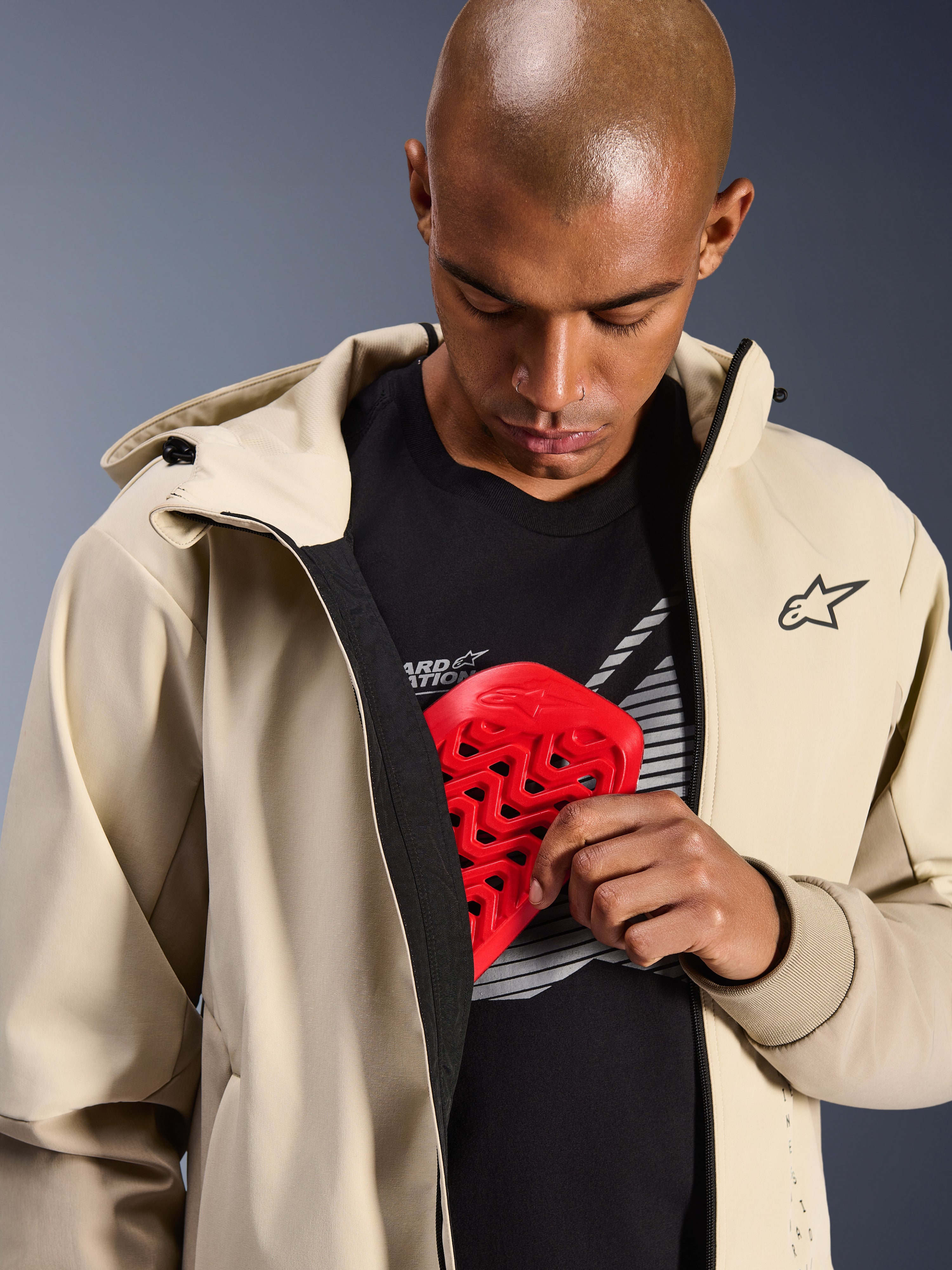 Alpinestars Radium Tech Hoodie i Mastic Aluminum, urban motorcykeljakke, model der demonstrerer indvendig beskyttelseslomme med en rød Nucleon brystbeskytter, vindtæt tech-shell med et afslappet hættetrøjedesign og Alpinestars-branding