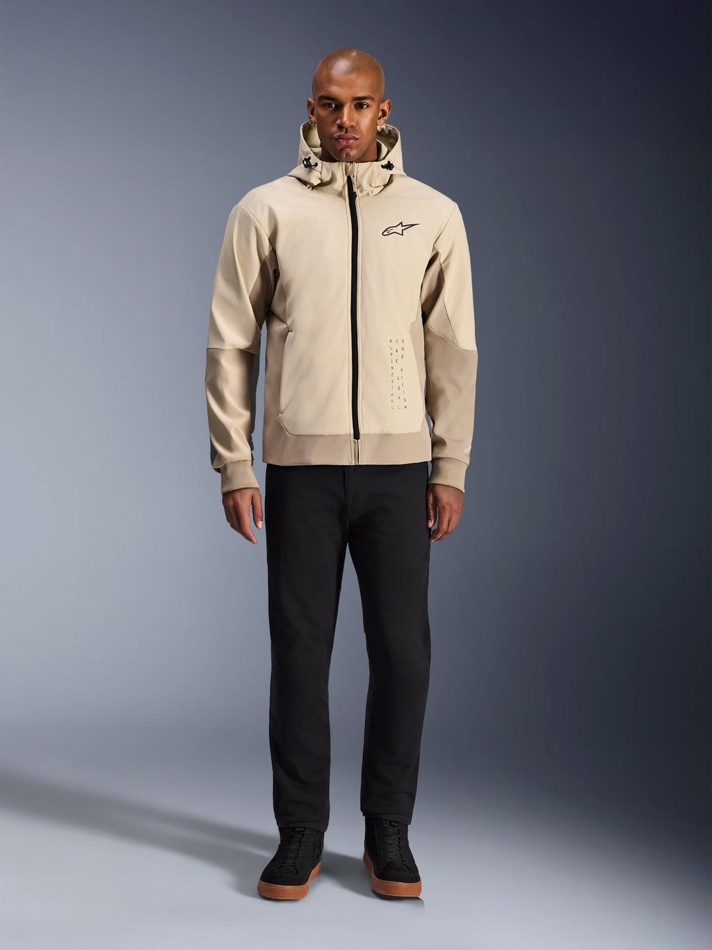 Alpinestars Radium Tech Hoodie i Mastic Aluminum, urban motorcykelhættetrøje båret af en mandlig model med sorte bukser og sorte støvler, med gennemgående sort lynlås, lille logo på brystet og atletisk pasform til bykørsel