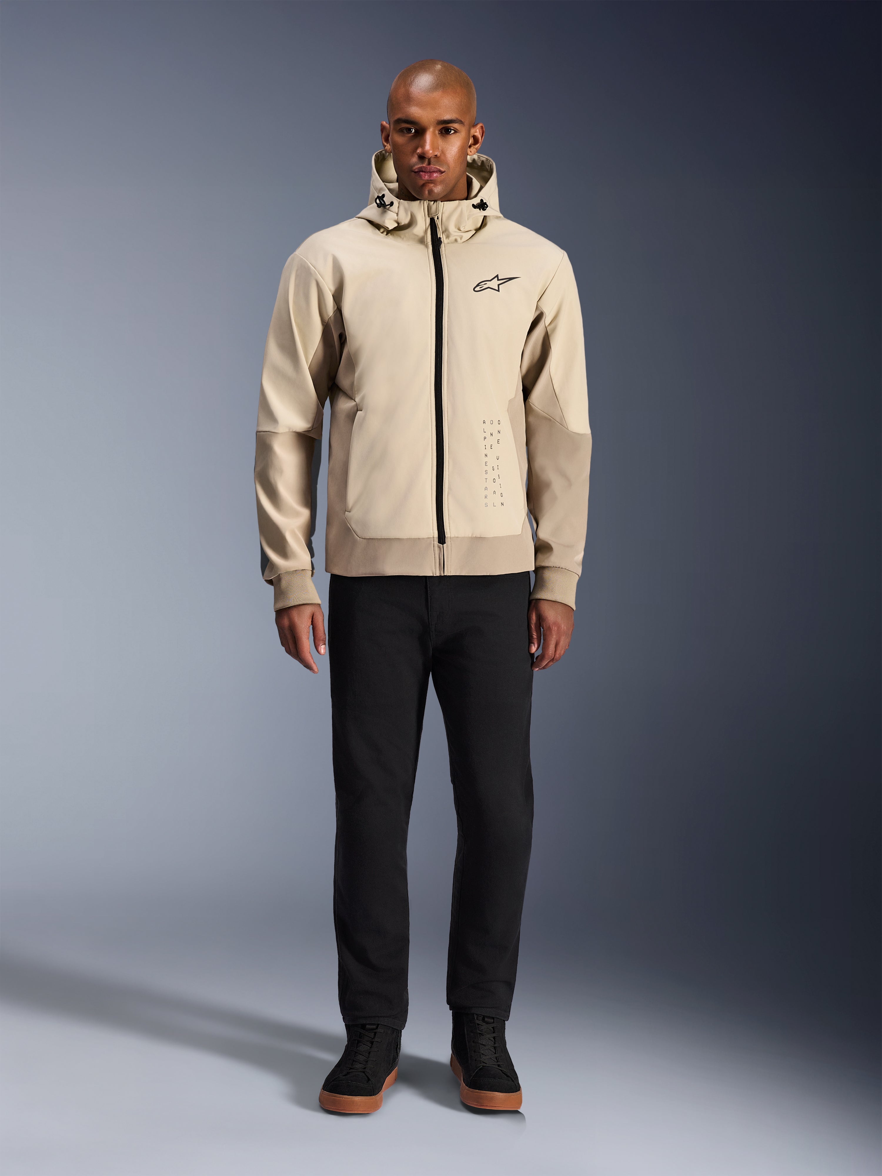 Alpinestars Radium Tech Hoodie i Mastic Aluminum, urban motorcykelhættetrøje båret af en mandlig model med sorte bukser og sorte støvler, med gennemgående sort lynlås, lille logo på brystet og atletisk pasform til bykørsel