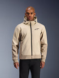 Alpinestars Radium Tech Hoodie i Mastic Aluminum, lysebeige og sandfarvet urban motorcykeljakke, sort lynlås foran og lille logo på brystet, vist på en mand i sorte bukser, teknisk vindtæt skal med moderne streetwear-styling