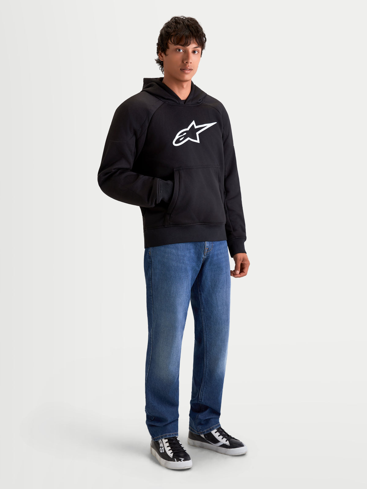 Alpinestars Ageless hættetrøje, herre-urban motorcykelhættetrøje i sort, frontvisning af model iført afslappede denimjeans, med et fremtrædende hvidt Astar-logo på brystet