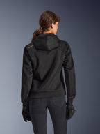 Alpinestars Stella Chrome Superairflow Hoodie, set bagfra af kvinde iført sort teknisk 3D-mesh motorcykelhættetrøje, har konstrueret hætte og kobberfarvet logo på skulderen, kombineret med sorte motorcykelhandsker og bukser.