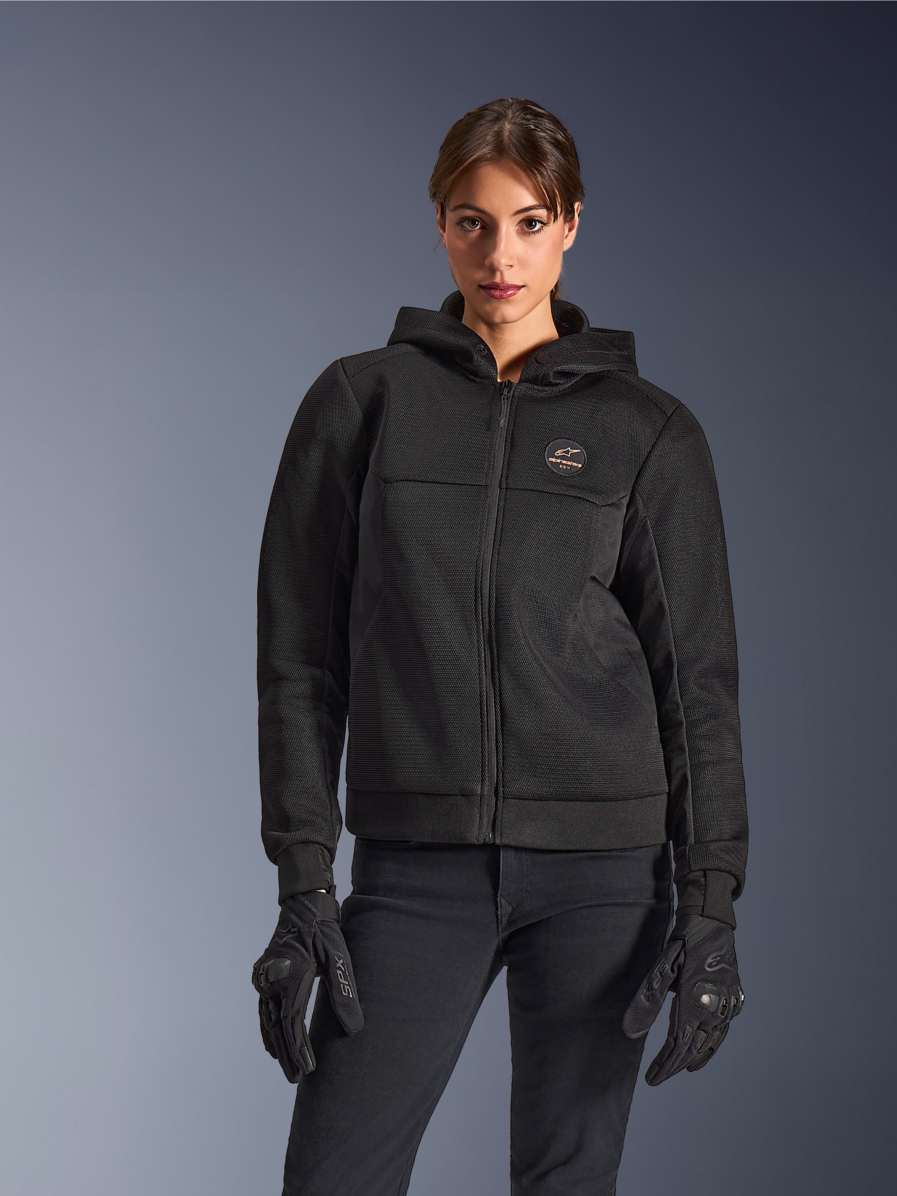 Alpinestars Stella Chrome Superairflow Hoodie, motorcykelhættetrøje til damer, sort, hættejakke med logo på brystet og centreret lynlås, vist med sorte handsker, strømlinet moderne design til bykørsel