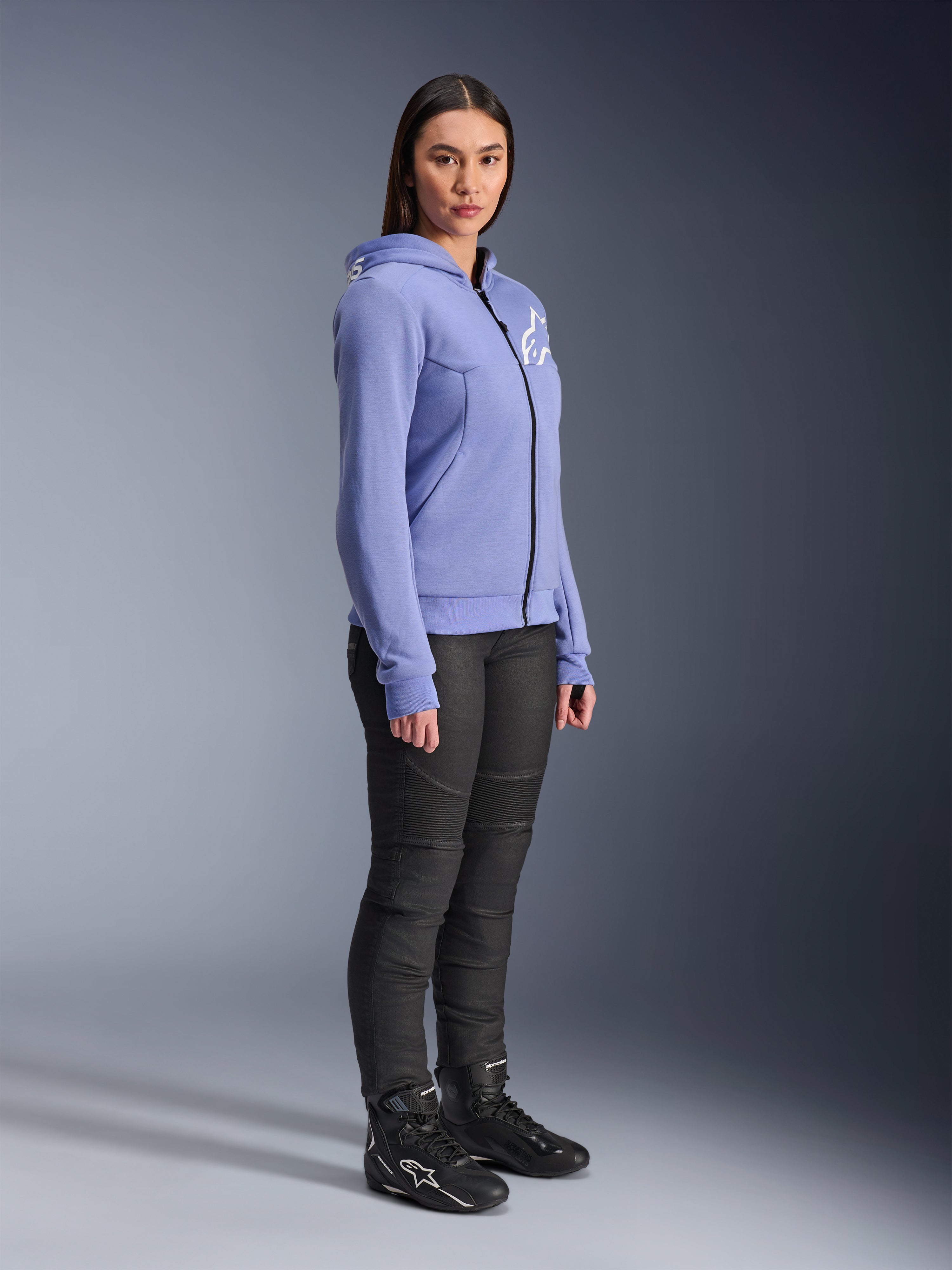 Alpinestars Stella Chrome V2 Sport Hoodie til kvinder, motorcykel-hættetrøje i blåviolet med hvidt Alpinestars-logo på brystet, båret af en model med sorte MC-bukser og sorte motorcykelstøvler, urbant køreudstyr til kvinder