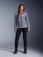 Alpinestars Stella Chrome V2 Sport Hoodie, Gray Heather Pink Fluo, båret af en kvinde med sorte bukser og støvler, med et lyserødt Alpinestars-stjernelogo på brystet, urbant motorcykeludstyr med gennemgående lynlås, letvægts tech-fleece med en afslappet atletisk pasform.