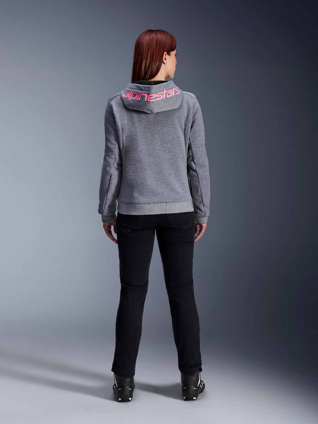 Alpinestars Stella Chrome V2 Sport Hoodie, motorcykelhættetrøje til kvinder, Gray Heather og Pink Fluo, set bagfra viser lyserødt Alpinestars-logo på hætten, båret med sorte kørebukser og støvler, afslappet motorcykelbeklædning til kvinder