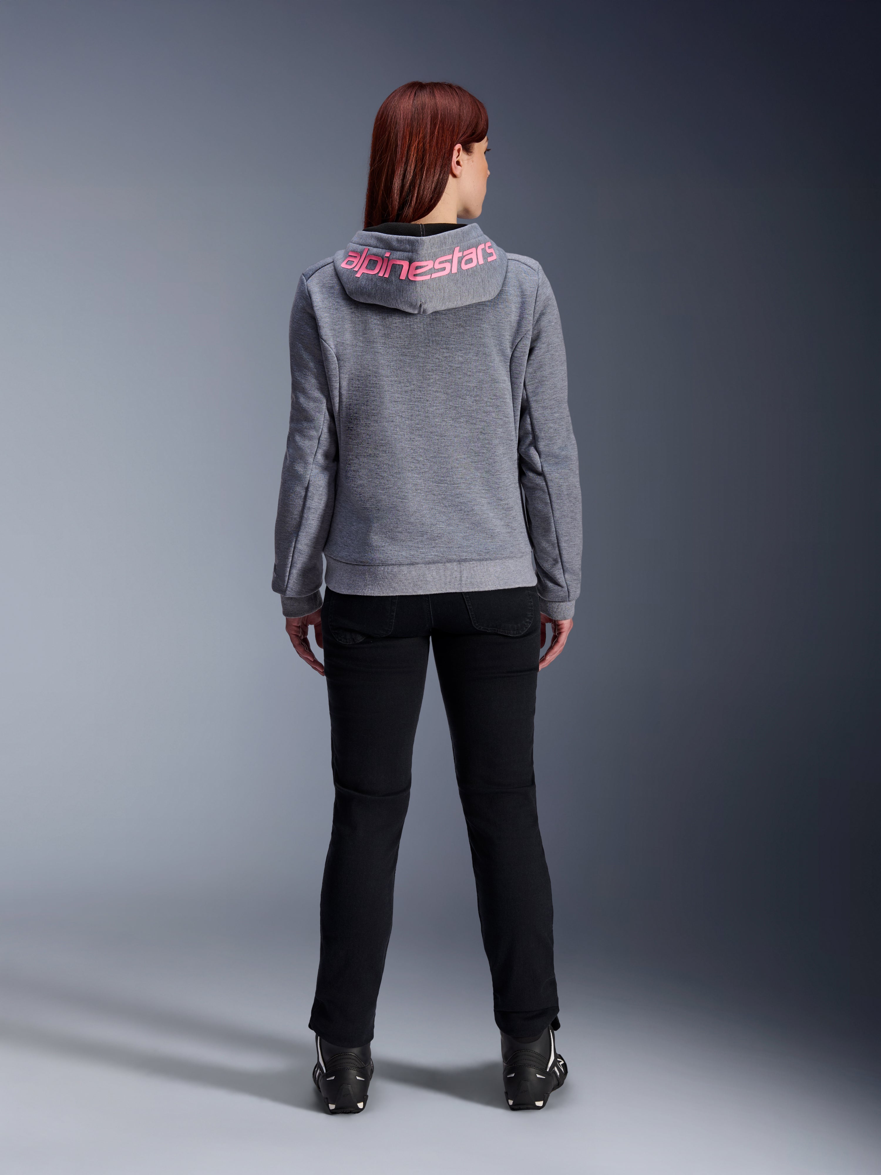 Alpinestars Stella Chrome V2 Sport Hoodie, motorcykelhættetrøje til kvinder, Gray Heather og Pink Fluo, set bagfra viser lyserødt Alpinestars-logo på hætten, båret med sorte kørebukser og støvler, afslappet motorcykelbeklædning til kvinder