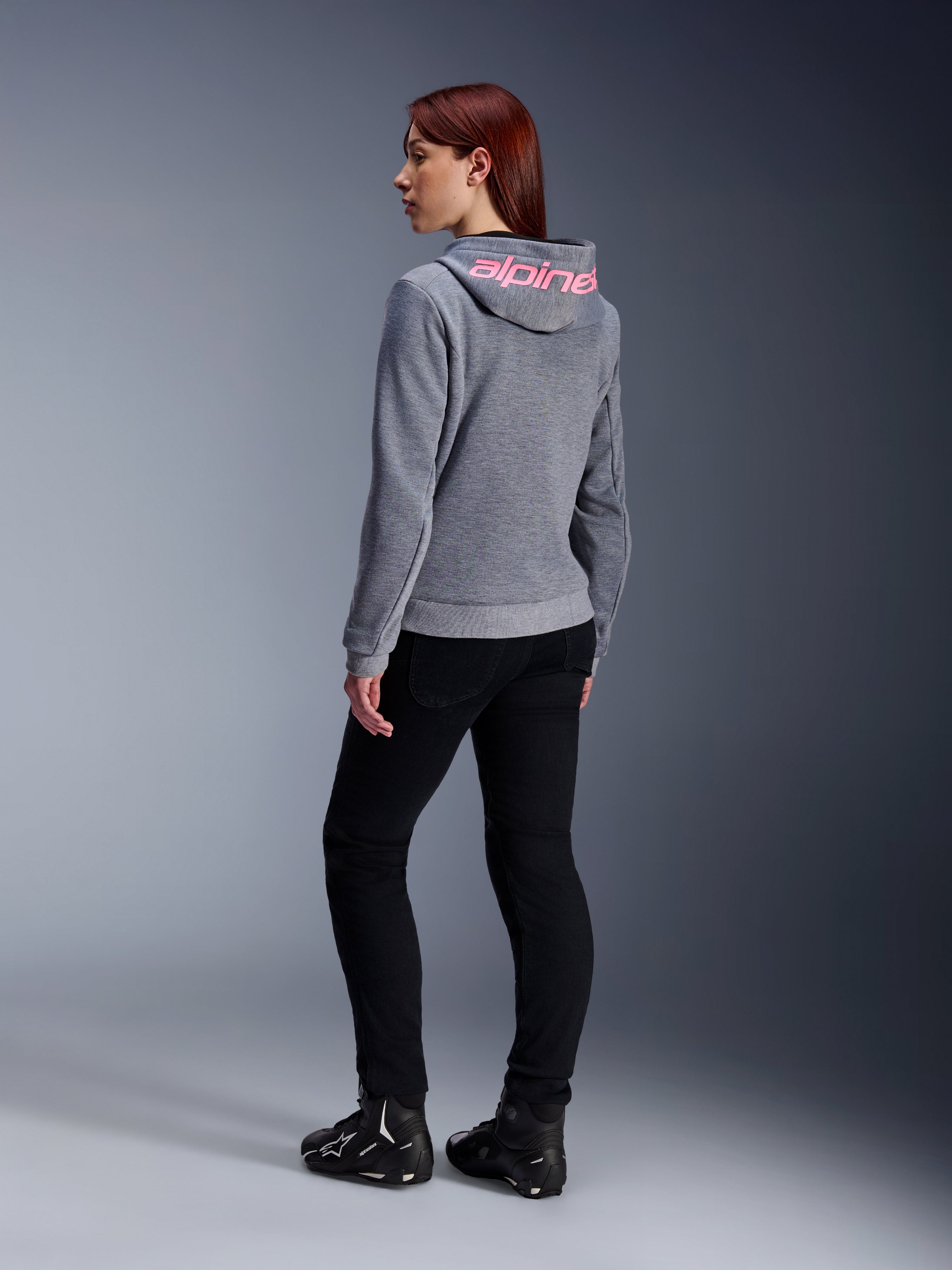 Alpinestars Stella Chrome V2 Sport Hoodie, motorcykelhættetrøje til damer, gråmeleret med Pink Fluo-branding på hætten, set bagfra, båret med sorte bukser og køresko, afslappet urban street-stil med motorcykelbeskyttelse