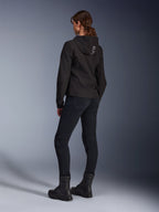 Alpinestars Stella Radium Tech Hoodie, sort urban kørehættetrøje til kvinder, set bagfra med 'ALPIN'-branding på hætten, kombineret med sorte tekniske kørebukser og sorte støvler, letvægts vindtæt tech-shell