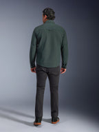Alpinestars Bryon vandafvisende overshirt i Dark Emerald, set bagfra på model, kombineret med mørkegrå motorcykelbukser og sorte køresko, viser et klassisk arbejdstøjsinspireret design med en lidt længere ryg for bedre dækning under kørsel.