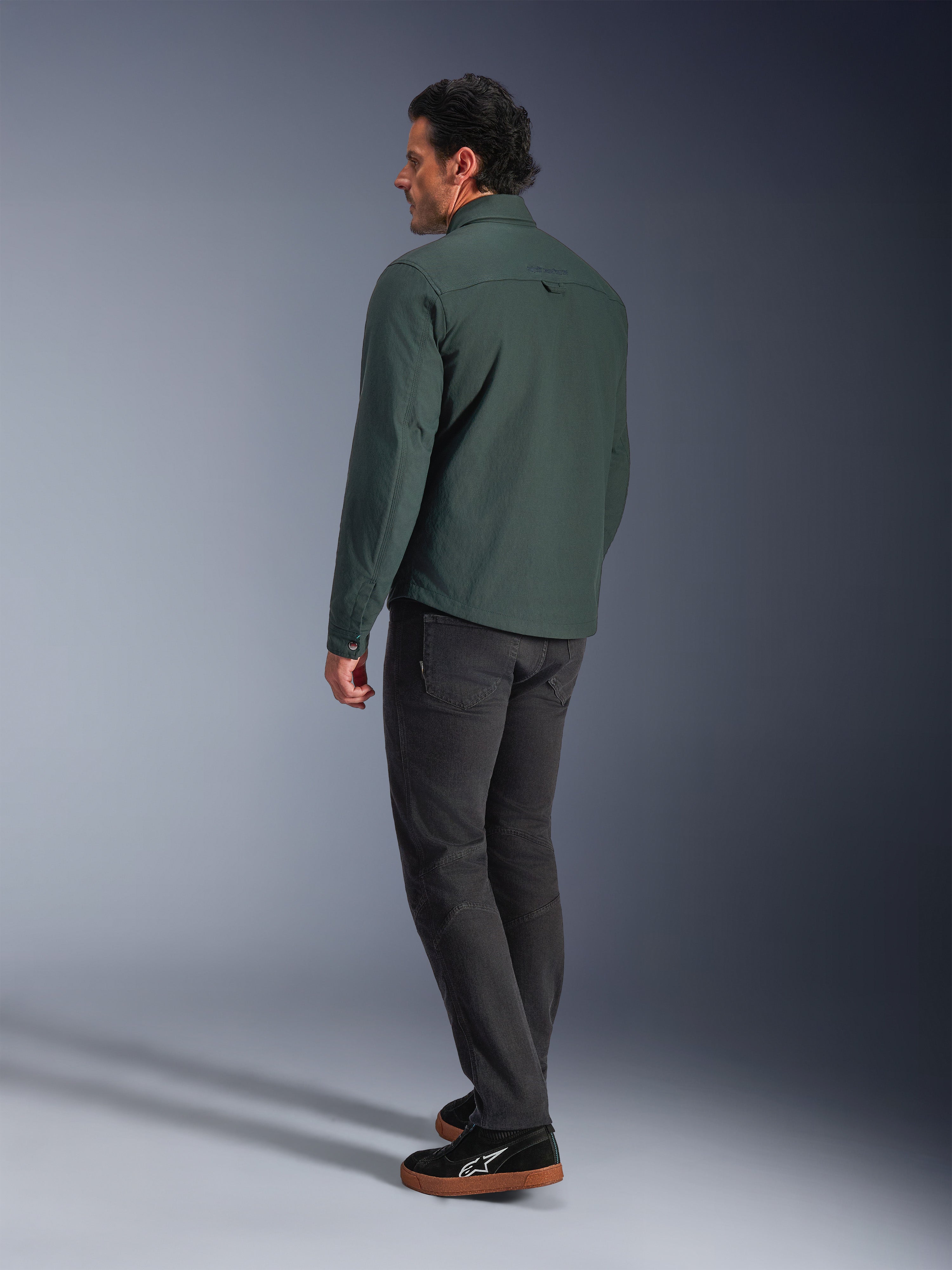 Alpinestars Bryon Water Resistant Overshirt, mørk smaragdgrøn, urban motorcykeljakke set bagfra, båret med mørke bukser og sorte sneakers, moderne arbejdstøjsinspireret design.