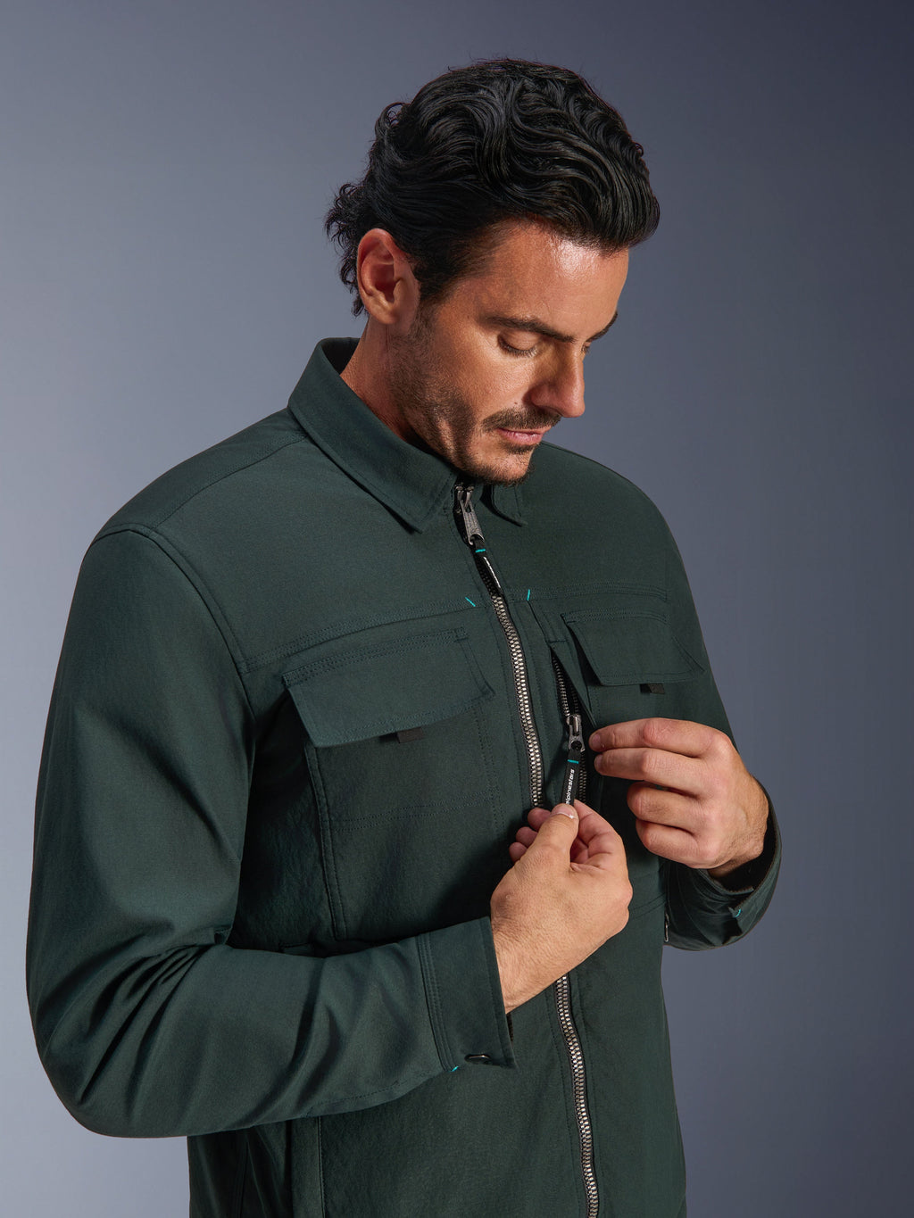 Alpinestars Bryon WR Overshirt i Dark Emerald, urban motorcykeljakke, båret af en mand der demonstrerer den lodrette brystlomme med lynlås og cargo-lommer, med en slidstærk tekstur i vokset lærred og arbejdstøjsinspireret design