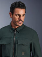 Alpinestars Bryon vandafvisende overshirt i Dark Emerald, nærbillede af en mand iført den urbane motorcykeljakke, tekstur af vokset lærred, frontlynlås med diskrete blågrønne accenter, brystlommer og logo-patch.