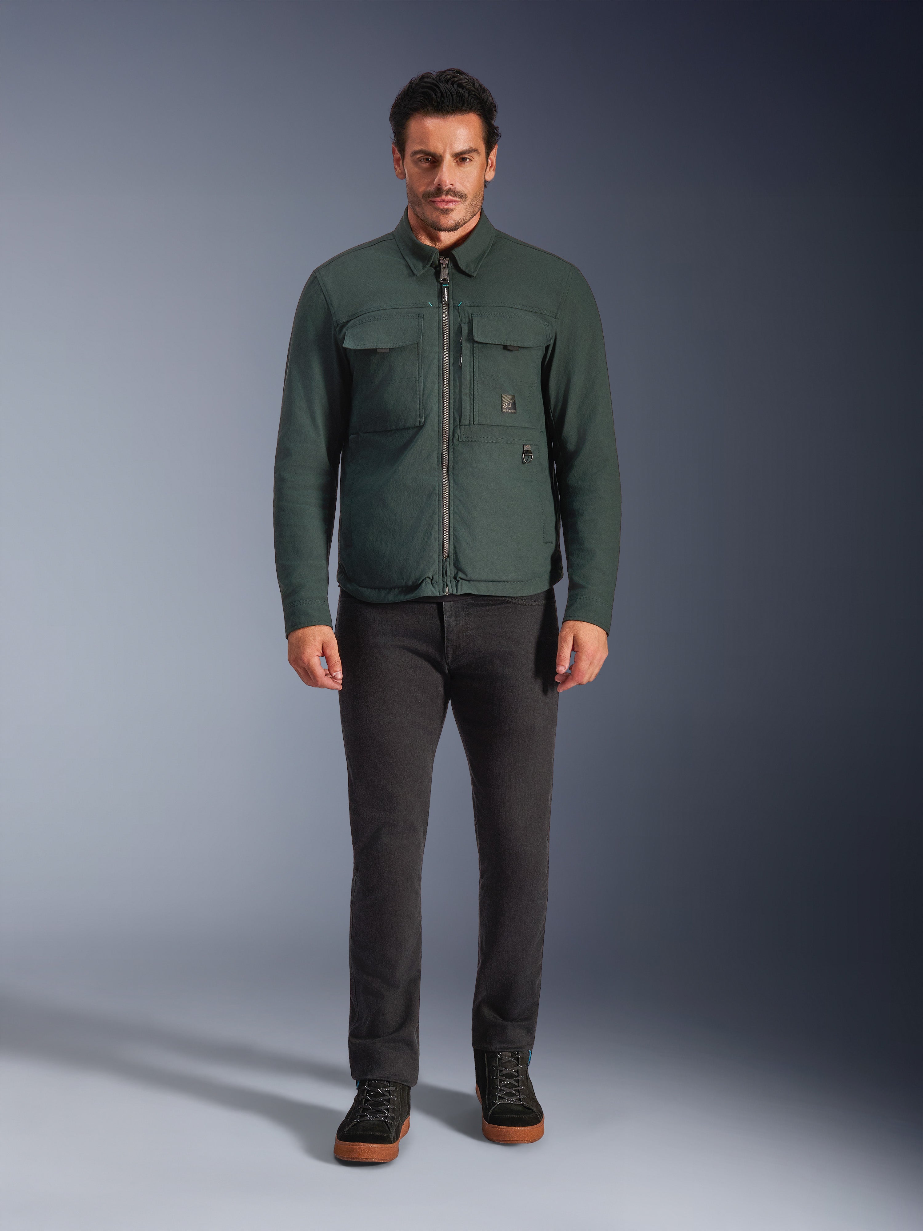 Alpinestars Bryon WR Overshirt, vandafvisende motorcykeljakke, Dark Emerald, båret med sorte bukser og sorte støvler, med konstruktion i vokset lærred, brystlommer og et moderne urbant design.