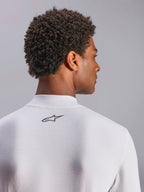 Alpinestars ZX Evo V3 Top, langærmet undertrøje til motorsport, hvid, nærbillede af nakkeområdet med sort Alpinestars-logo, teknisk flammehæmmende materiale, båret af model med mørkt krøllet hår