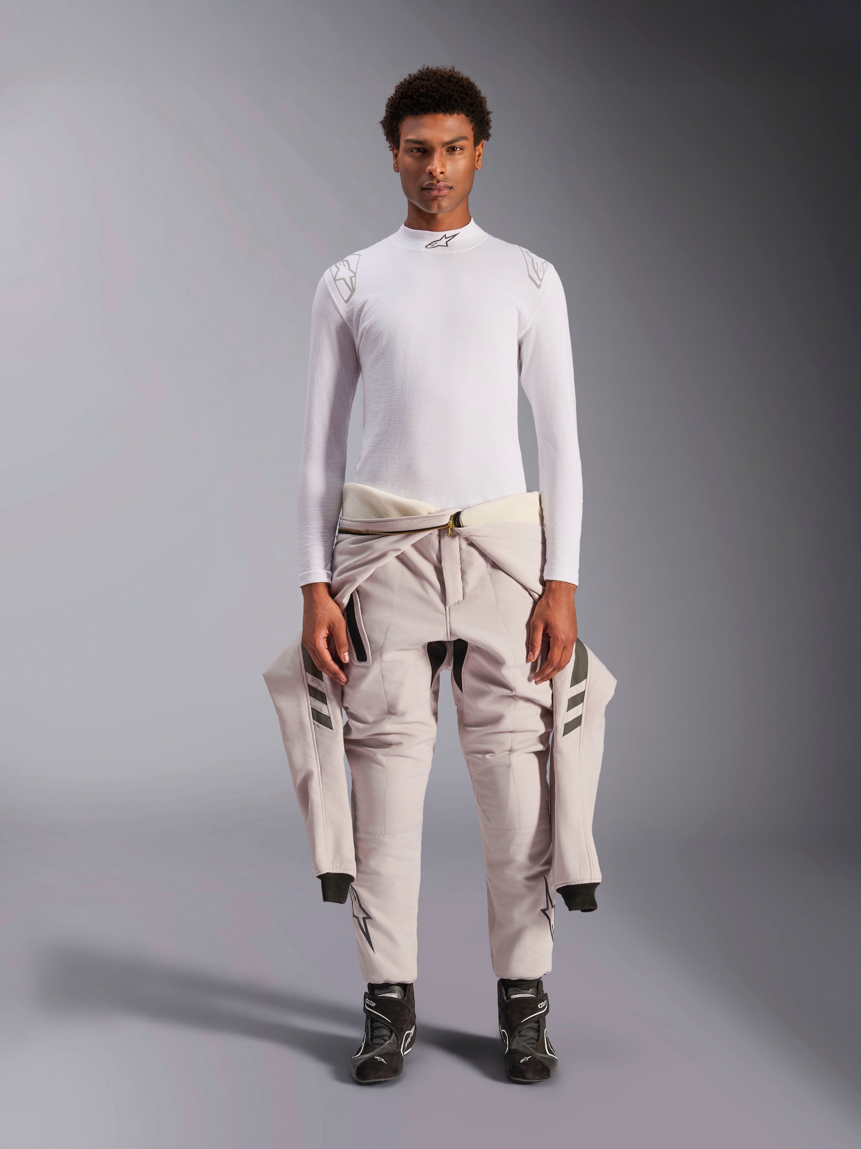 Alpinestars ZX Evo V3 Top, langærmet, hvid, base layer til bilsport båret med en lys køredragt bundet om taljen og sorte kørestøvler, med mock neck med logo og branding på skuldrene, professionelt flammebestandigt motorsport-undertøj