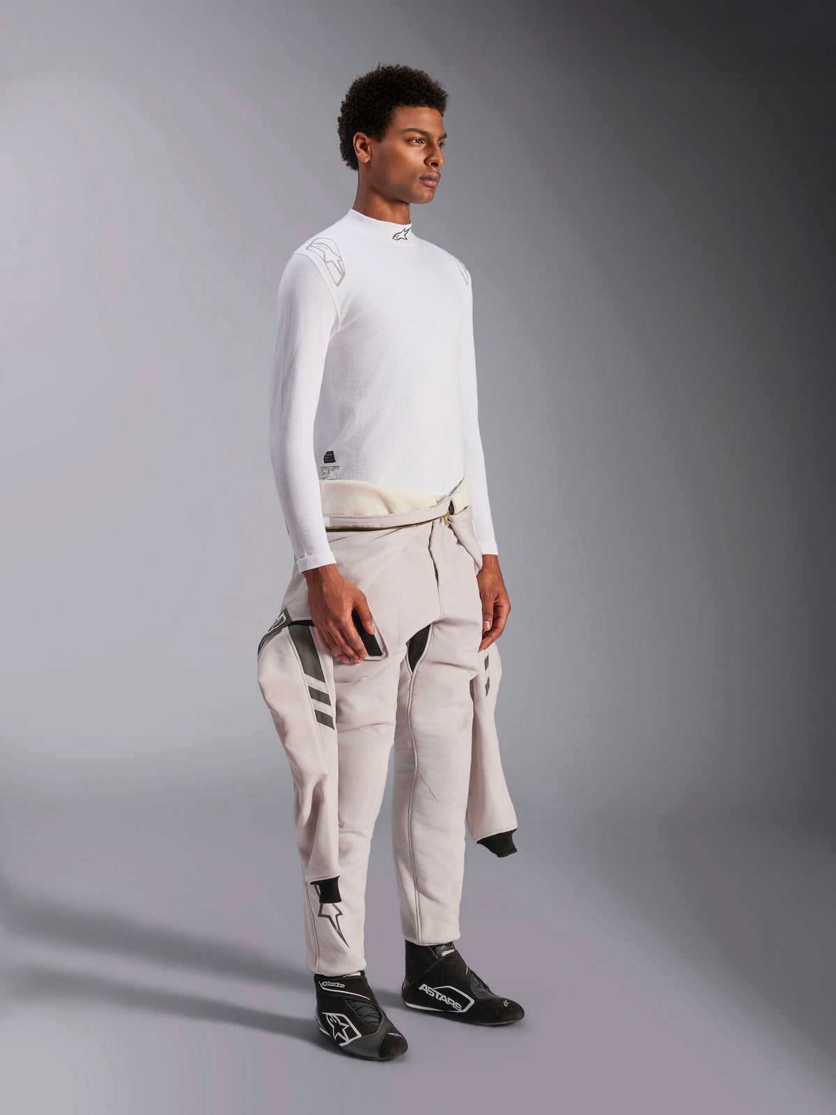 Alpinestars ZX Evo V3 Langærmet Top, hvid flammebestandig base layer til bilvæddeløb, bæres af en model med en køredragt bundet om taljen, letvægts tech-lag med høj hals og logodetalje.
