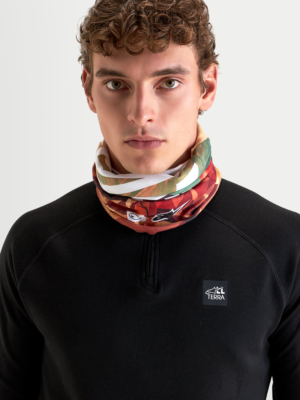 Alpinestars Buff Peaks Primaloft halsedisse, jordbrun og flerfarvet mønstret halsedisse båret af model i sort langærmet trøje, med let PrimaLoft-isolering til all-terrain motorcykelkørsel