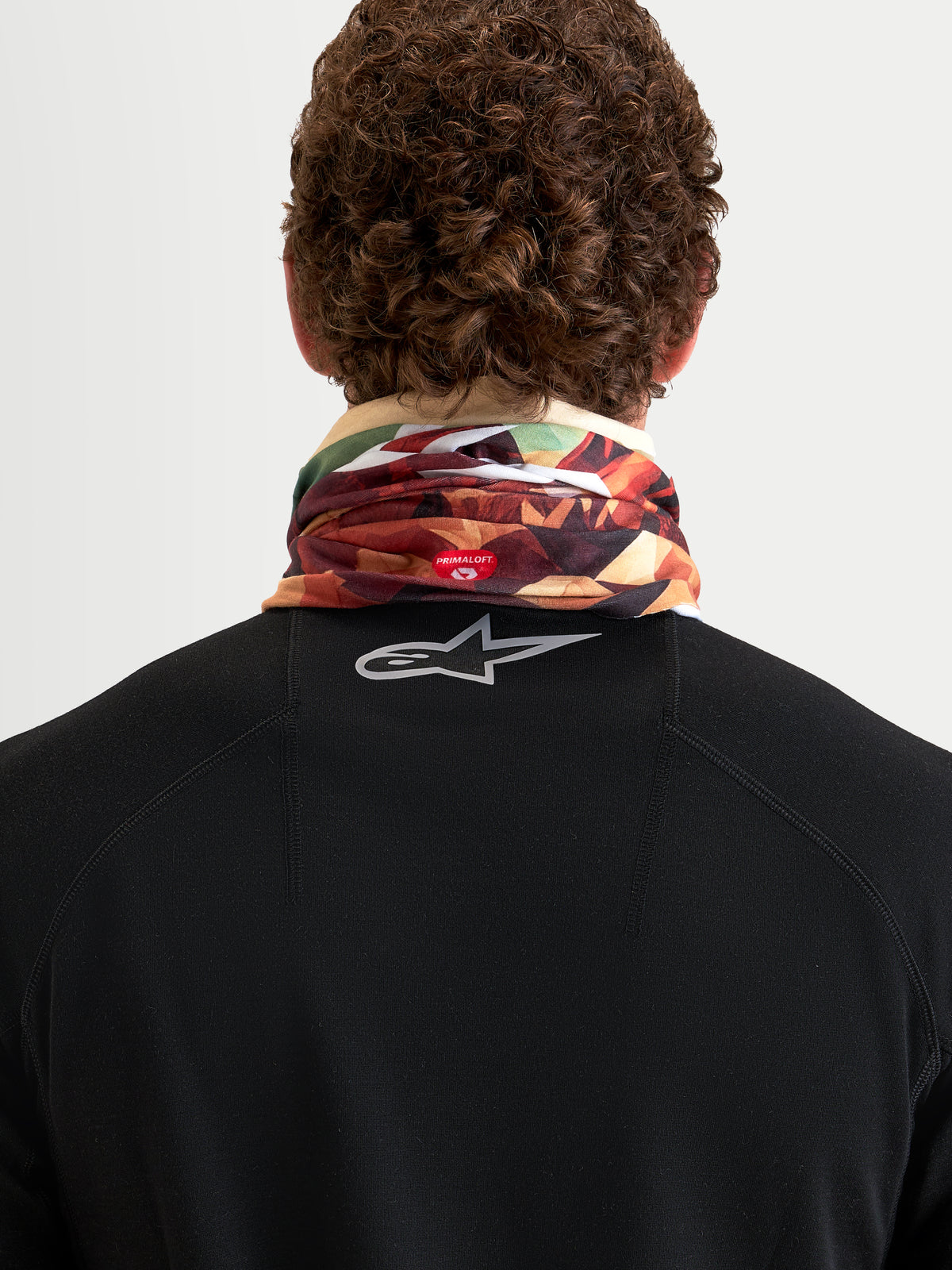 Alpinestars Buff Peaks PrimaLoft halsedisse, jordbrun og multifarvet, set bagfra på en model der viser isoleret rørstrikket konstruktion med PrimaLoft-branding og åndbart performance-udstyr