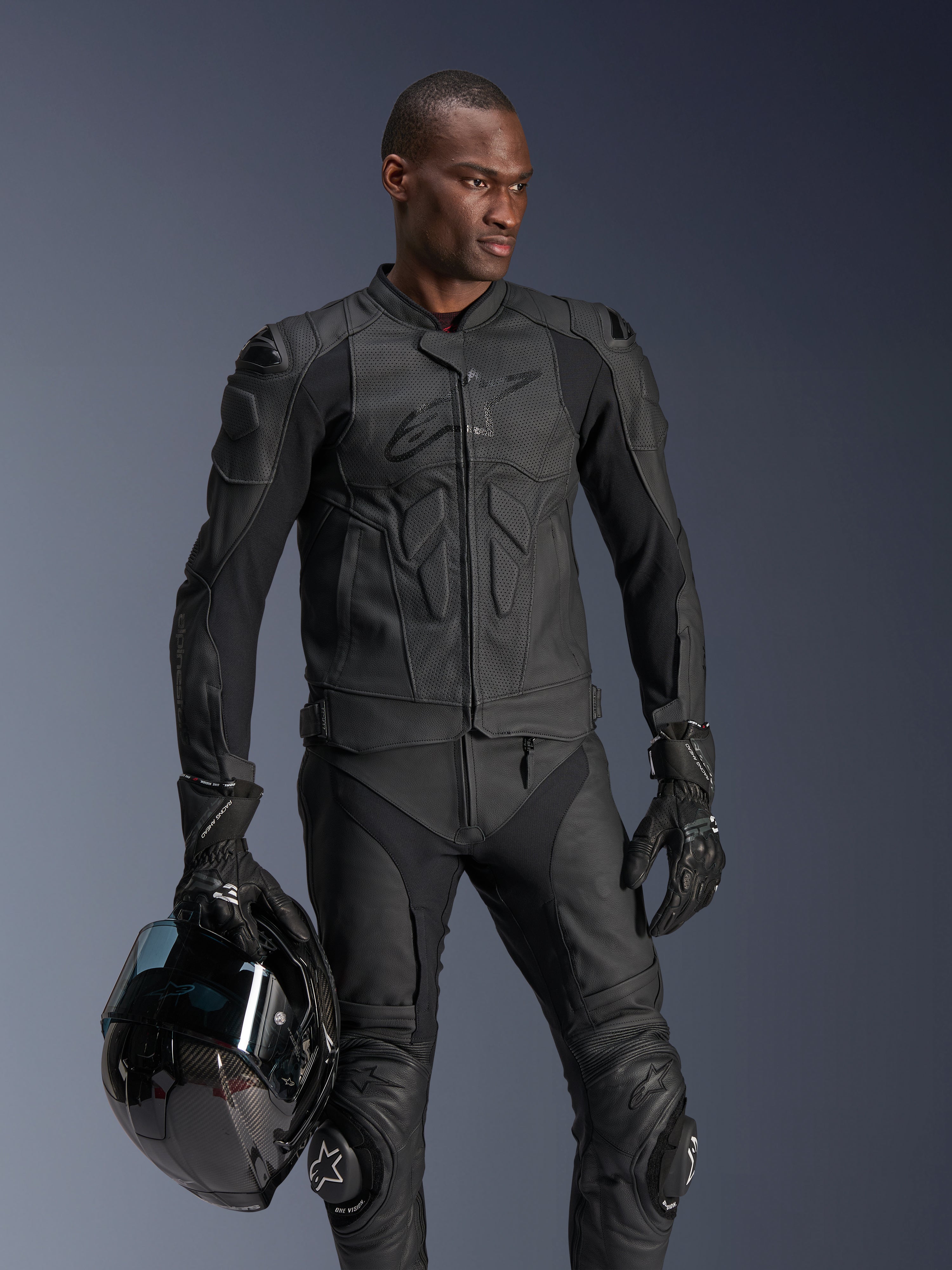 Alpinestars Dusk Airflow læderjakke, sort, mandlig kører med matchende læderbukser og handsker, holder en sort hjelm, med perforerede læderpaneler og integreret beskyttelse til sportslig motorcykelkørsel
