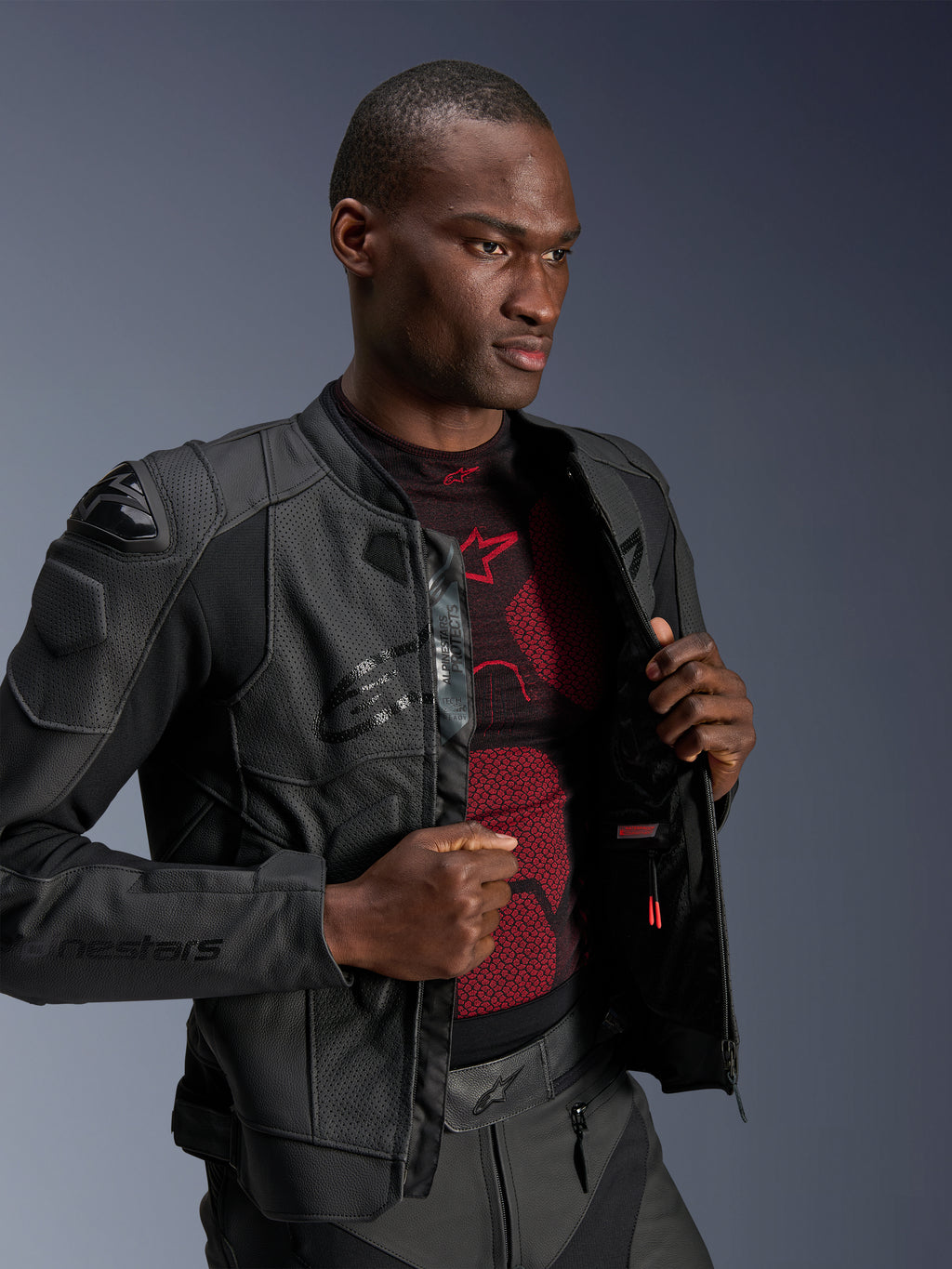 Alpinestars Dusk Airflow læderjakke, sort, båret af en mandlig model over et rødt og sort basislag, med perforerede læderpaneler, eksterne DFS-skulderskydere og en sportslig pasform.