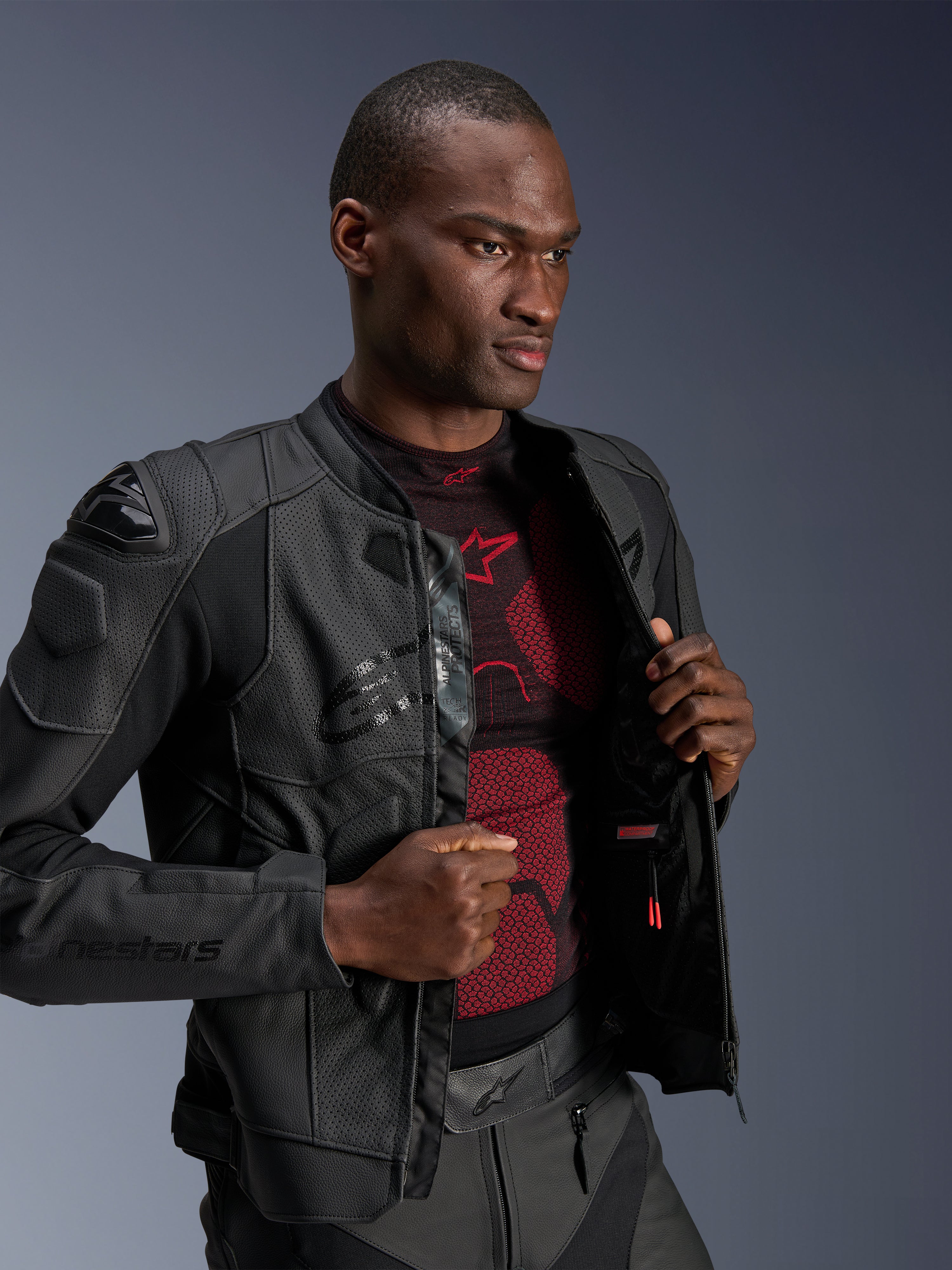 Alpinestars Dusk Airflow læderjakke, sort, båret af en mandlig model over et rødt og sort basislag, med perforerede læderpaneler, eksterne DFS-skulderskydere og en sportslig pasform.