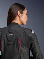 Kvinde iført Alpinestars Stella Dusk læderjakke, sort læder med Diva Pink-detaljer og hvidt logo på skulderen, set bagfra med DUSK-branding og harmonika-strækpaneler, sporty ergonomisk design