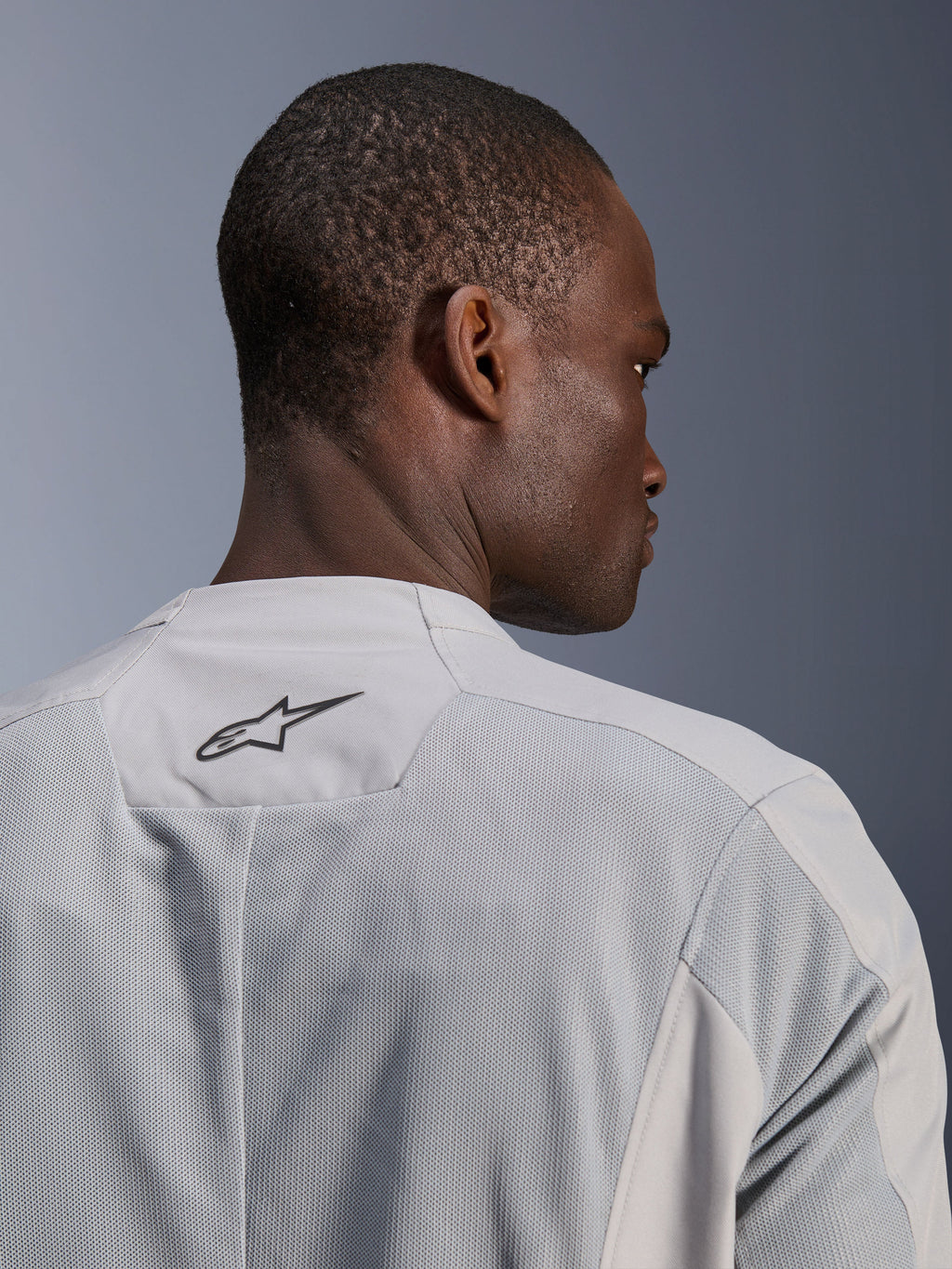 Alpinestars C-1 Air Jakke, sølvgrå tekstil-motorcykeljakke, nærbillede bagfra med tech-mesh-paneler til luftgennemstrømning, sort Alpinestars-logo på den øverste del af ryggen, urban rytter-æstetik