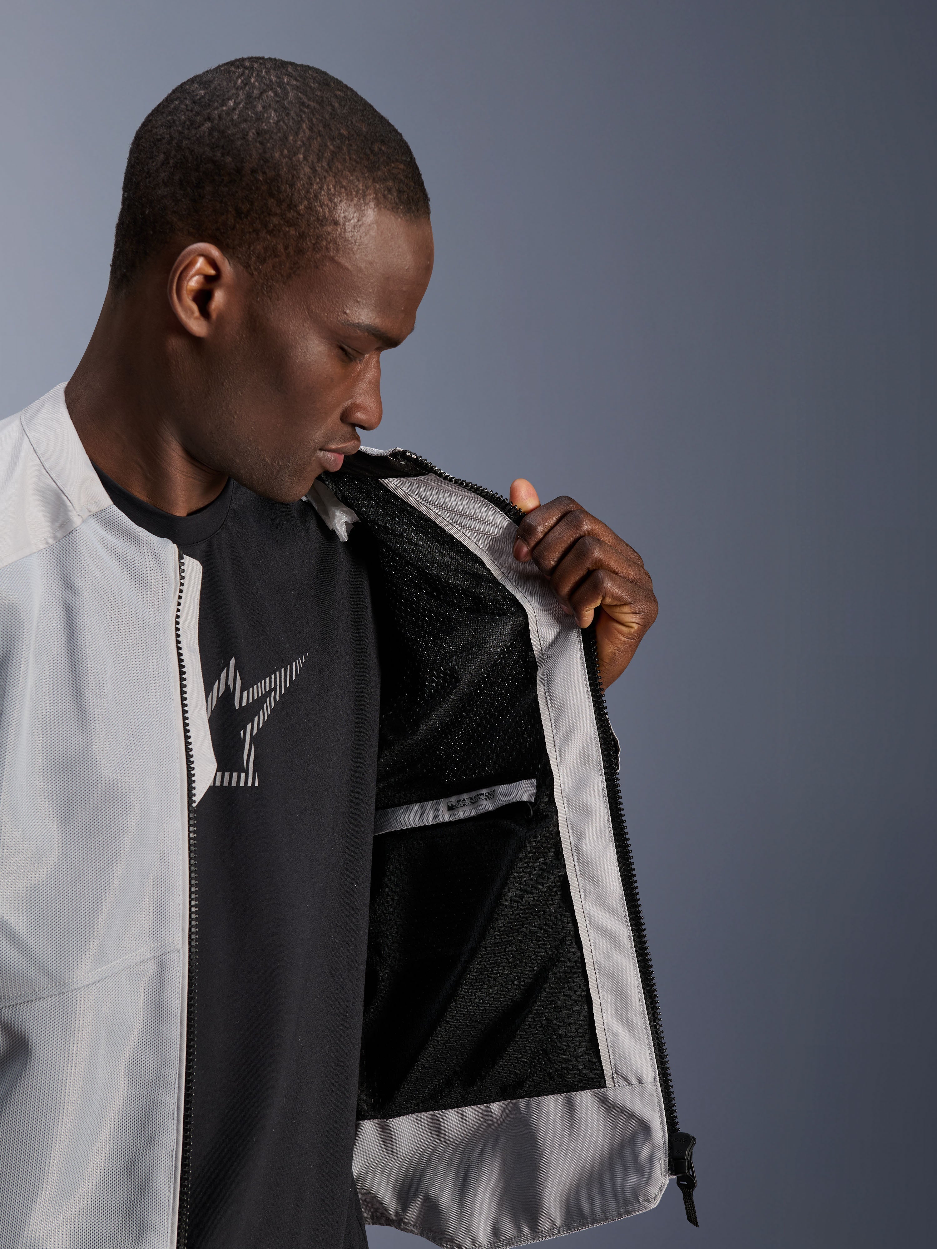 Mandlig model iført Alpinestars C-1 Air Jakke i sølv, der åbner fronten for at vise det sorte tech mesh-inderfor og en vandtæt inderlomme med lynlås.