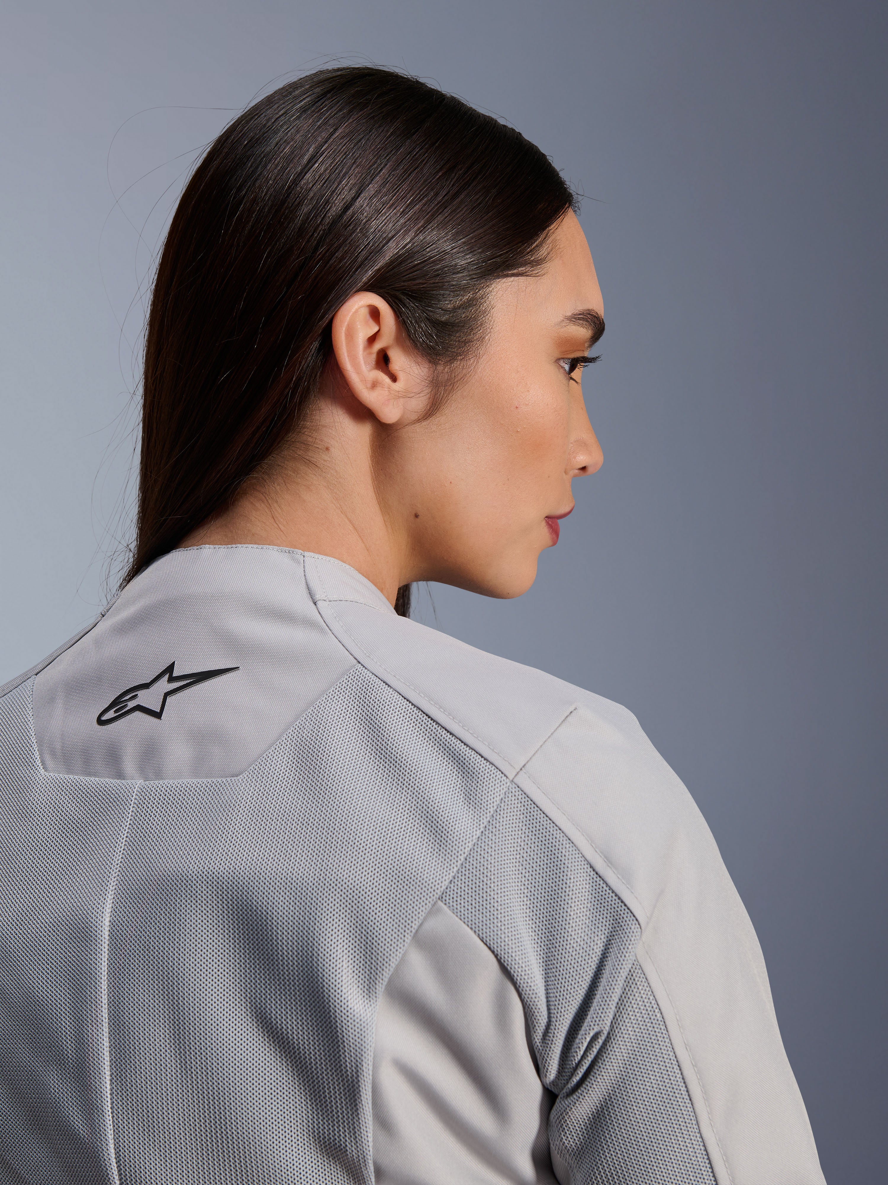 Kvinde iført Alpinestars Stella C-1 Air-jakke i sølv, nærbillede set fra siden og bagfra, sort Alpinestars-logo, tech mesh-ventilationspaneler, rent og moderne urbant motorcykeldesign