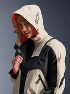 Alpinestars Molly Air-jakke i Black Almond, båret af en kvindelig model med hætten oppe, creme- og sort farveblokering, iøjnefaldende orange mesh-for, tekniske urbane designelementer, stjernelogo og lynlåsdetaljer