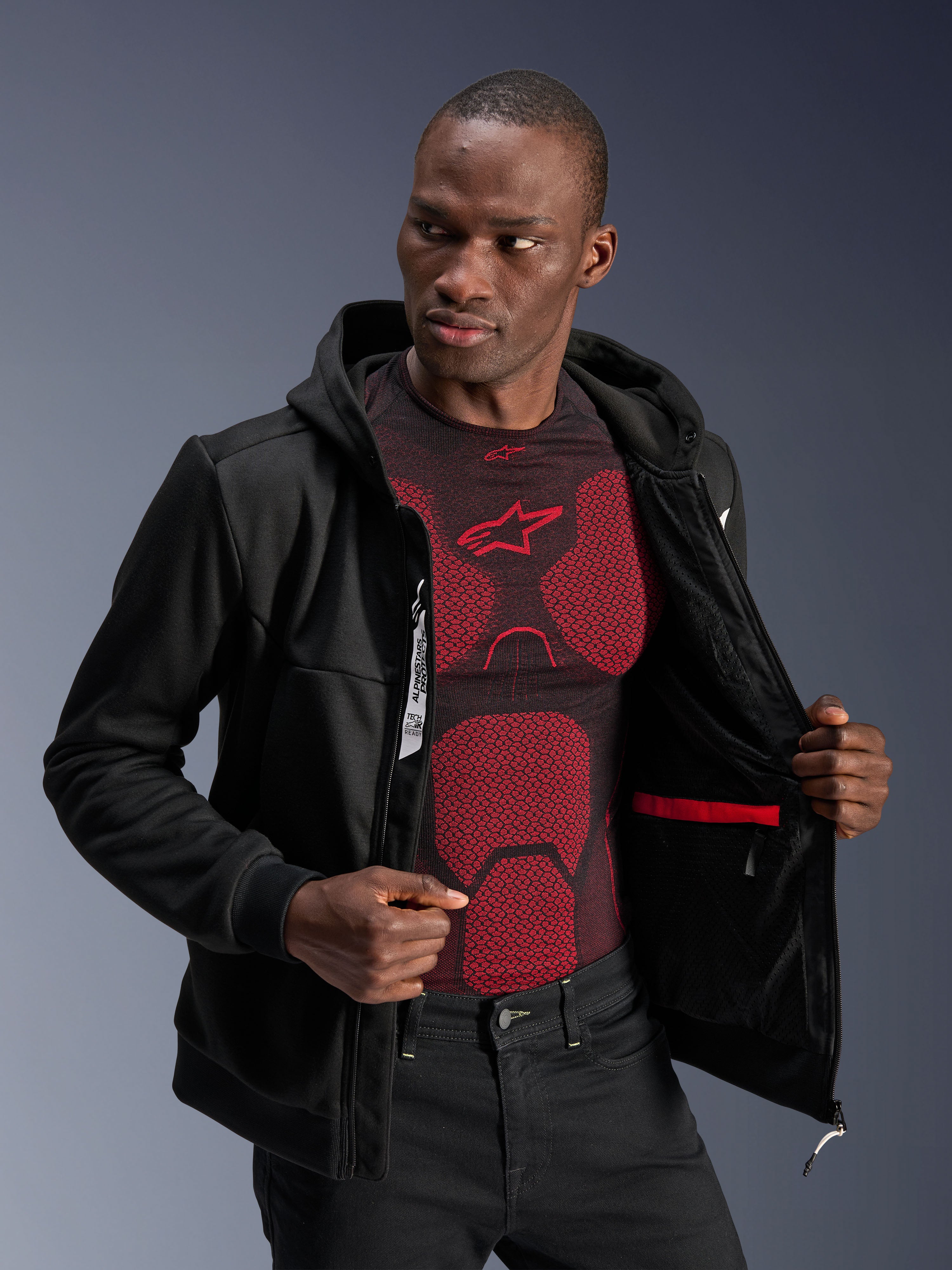 Alpinestars Chrome V2 Sport Hoodie, sort, mandlig model bærer jakken åben for at vise det indvendige for, rød vandtæt lomme og indvendig branding, båret over et rødt og sort basislag, afslappet urbant motorcykeludstyr