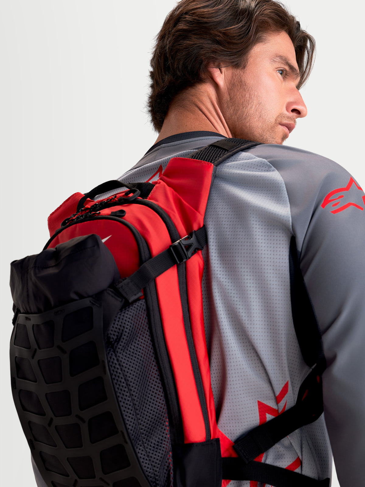 Alpinestars AT-9 rygsæk, sort og skarp rød MX-rygsæk, set bagfra hvor den bæres af en model med polstrede skulderstropper og letvægts tekstilkonstruktion