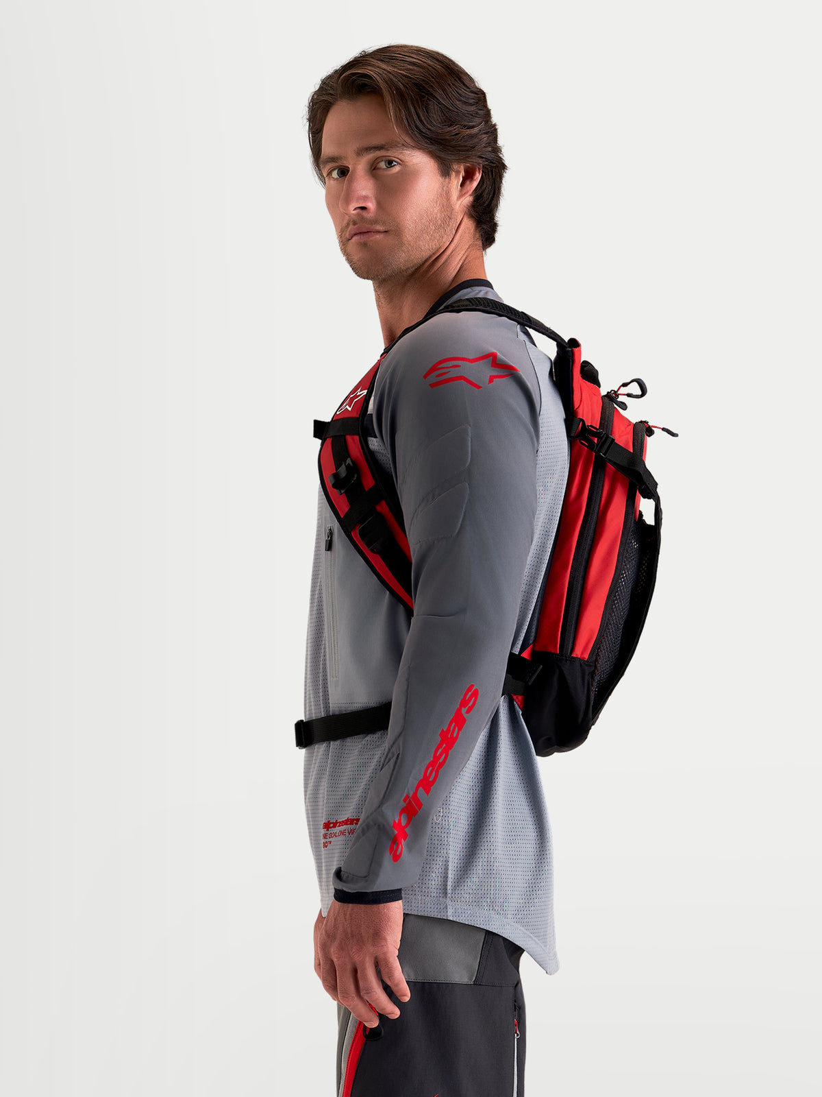 Alpinestars AT-9 rygsæk, sort og skarp rød motocross-rygsæk vist i sideprofil båret af mandlig model i matchende MX-udstyr med letvægtstekstilkonstruktion og ergonomisk bæresystem