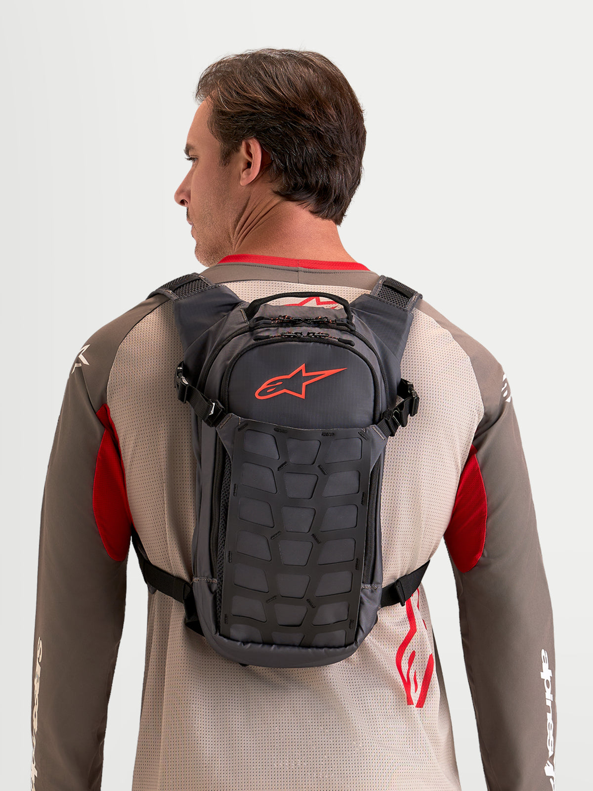 Alpinestars AT-9 Back Pack, motocross and everyday utility backpack worn by a model, walnut and deep gray textile construction, featuring organized storage compartments and a distinctive red Astar logo