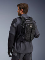 Alpinestars AT-15 rygsæk, adventure motorcykelrygsæk, sort og mørkegrå, båret af en kører i en grå jakke, med et teknisk design med MOLLE-webbing og 'TERRA'-branding, ergonomisk off-road udstyr