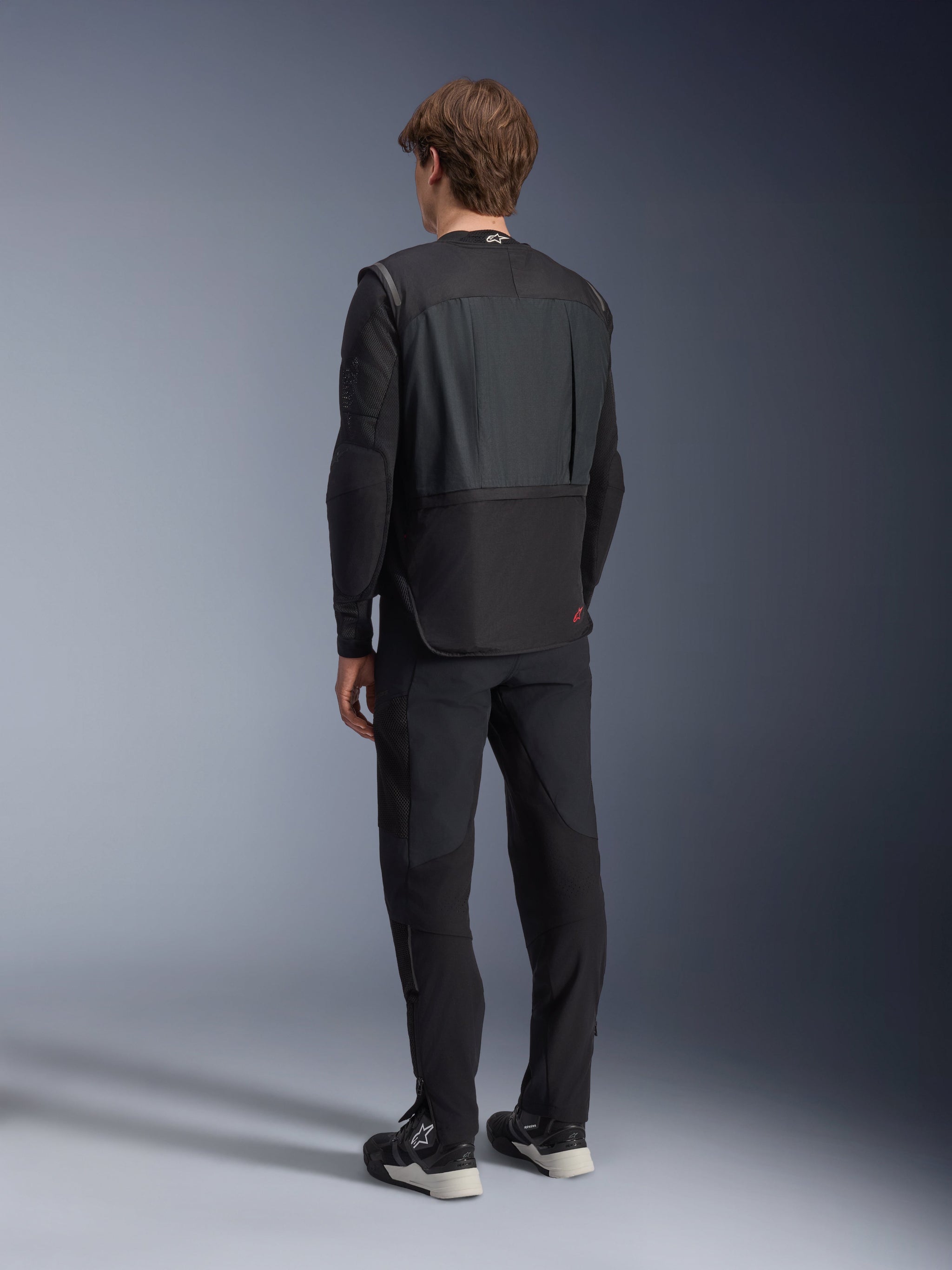 Alpinestars Tech-Air 3 V2 System, sort autonom motorcykel airbagvest, set bagfra båret af en model med sorte kørebukser, har en let og slank profil, rødt logo på den nederste del af ryggen, avanceret sikkerhedsudstyr til touring og pendling