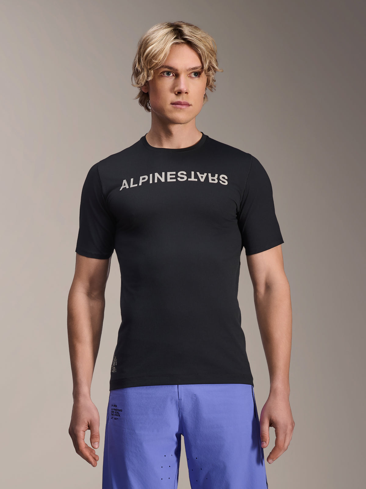 Alpinestars A-Aria Switch trøje, kortærmet MTB-trøje, sort med hvidt Alpinestars-navnetræk på brystet, båret af mandlig model med lilla shorts, letvægts performance-materiale til trail-kørsel