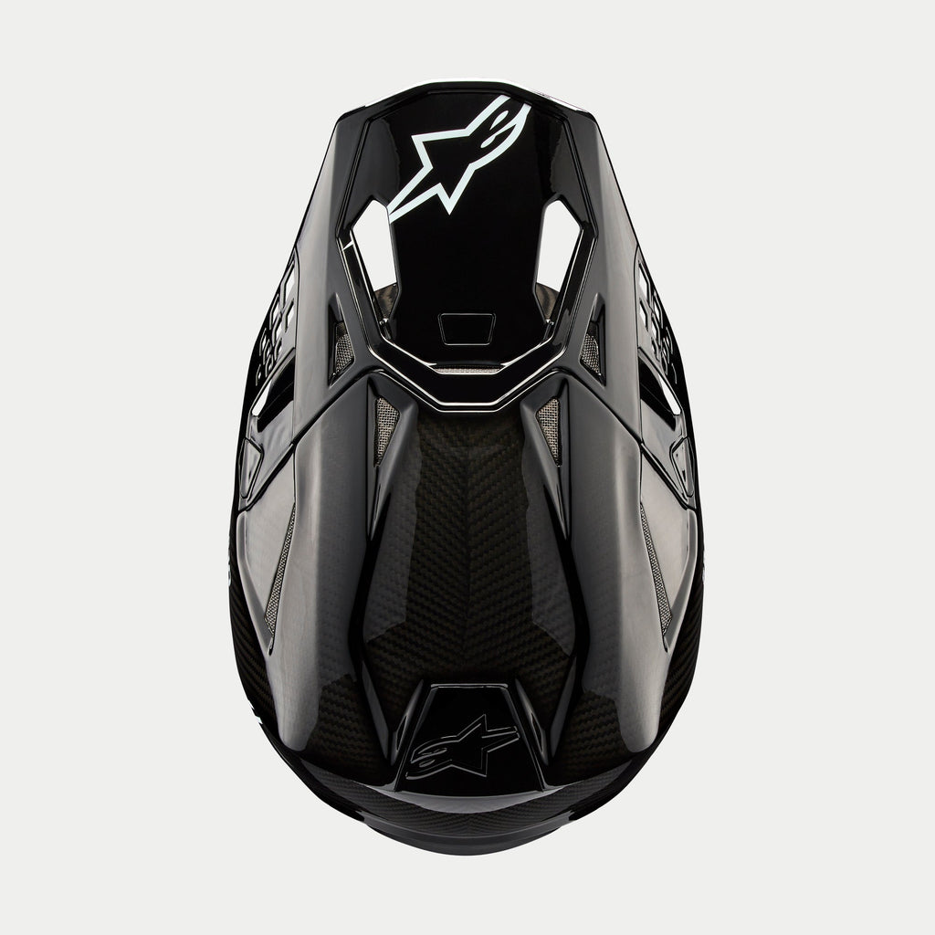 Alpinestars Supertech M10 Solid hjelm, motocrosshjelm, blank sort kulfiber, set ovenfra med synlig kulfibervævning, hvidt Astars-logo på visiret, slank aerodynamisk profil med integrerede ventilationsporte