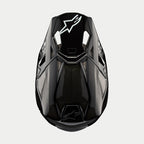 Alpinestars Supertech M10 Solid hjelm, motocrosshjelm, blank sort kulfiber, set ovenfra med synlig kulfibervævning, hvidt Astars-logo på visiret, slank aerodynamisk profil med integrerede ventilationsporte