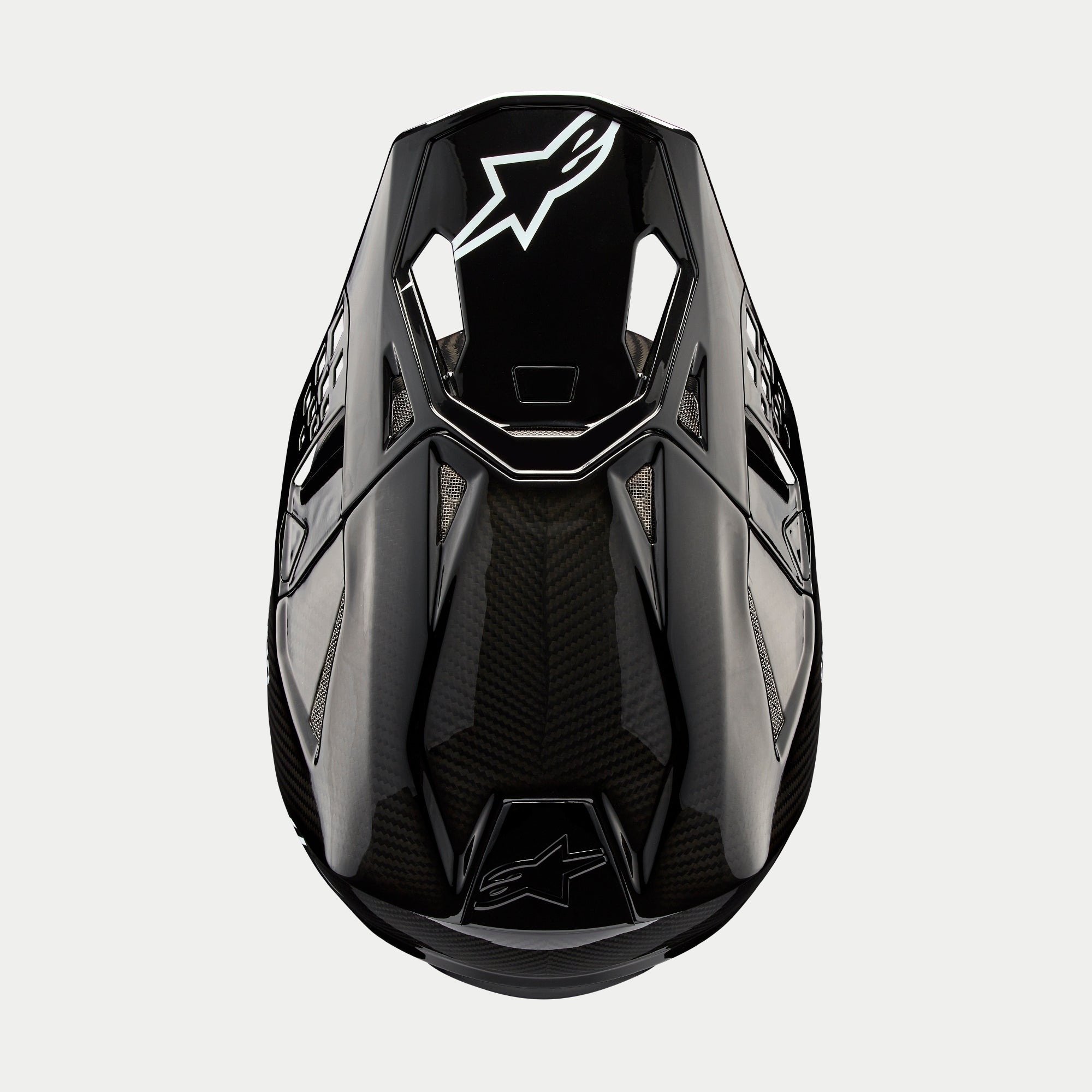 Alpinestars Supertech M10 Solid hjelm, motocrosshjelm, blank sort kulfiber, set ovenfra med synlig kulfibervævning, hvidt Astars-logo på visiret, slank aerodynamisk profil med integrerede ventilationsporte