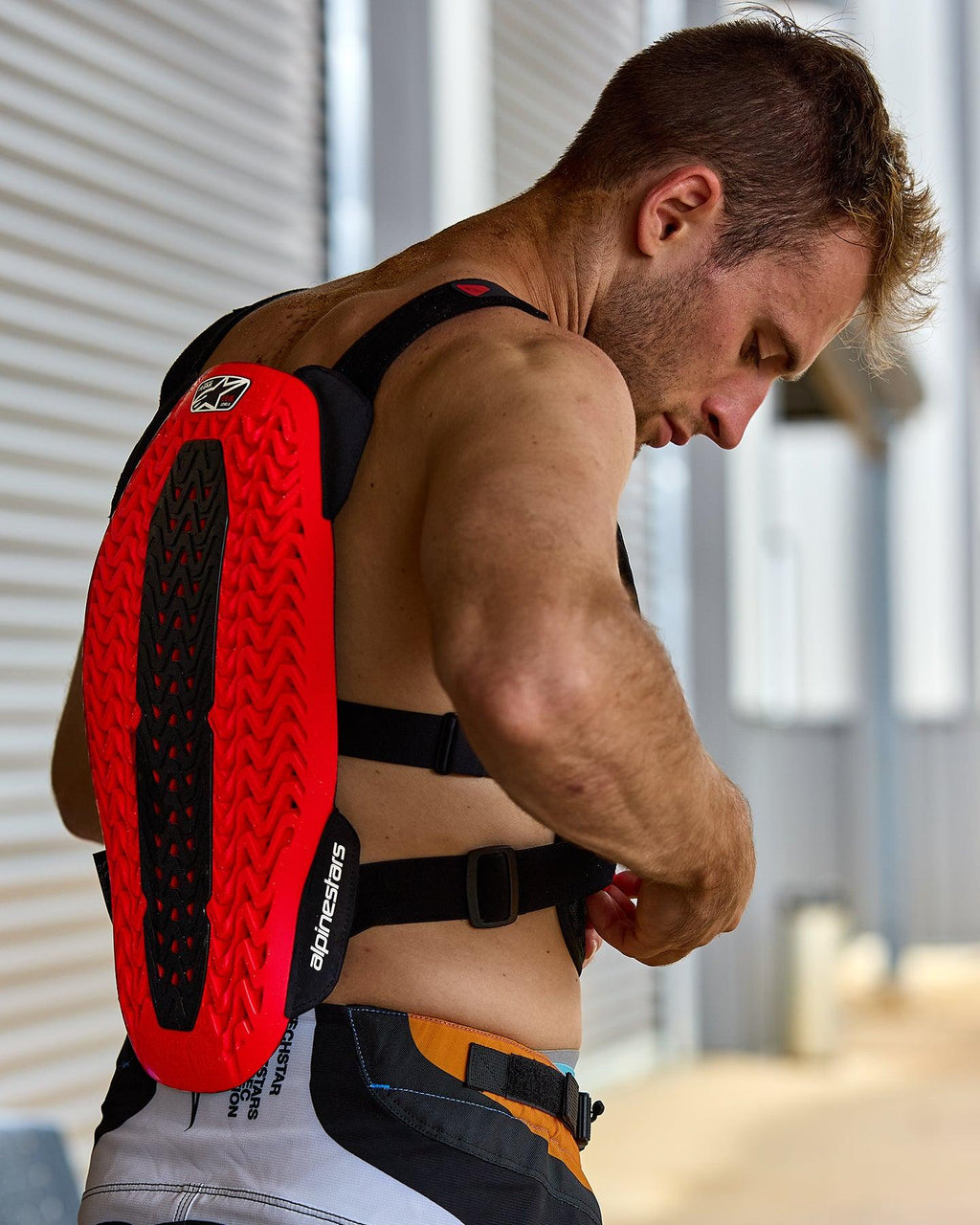 Alpinestars A-5 Plasma Brystbeskytter, rød og sort, med en tekstureret rygbeskytter med Nucleon PLASMA-teknologi, båret af en mand, der justerer sorte stropper, sidevisning, der fremhæver den beskyttende skal og det fleksible design til off-road kørsel