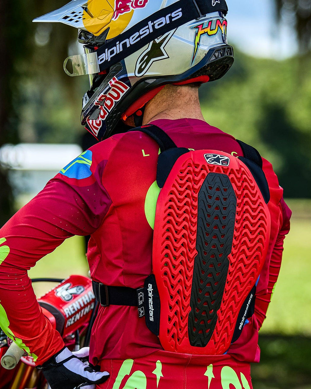 Alpinestars A-5 Plasma brystbeskytter, motocross-kører set bagfra, rød og sort rygbeskytter med ventileret bikagestruktur, båret over en rød langærmet trøje med en Red Bull-hjelm.