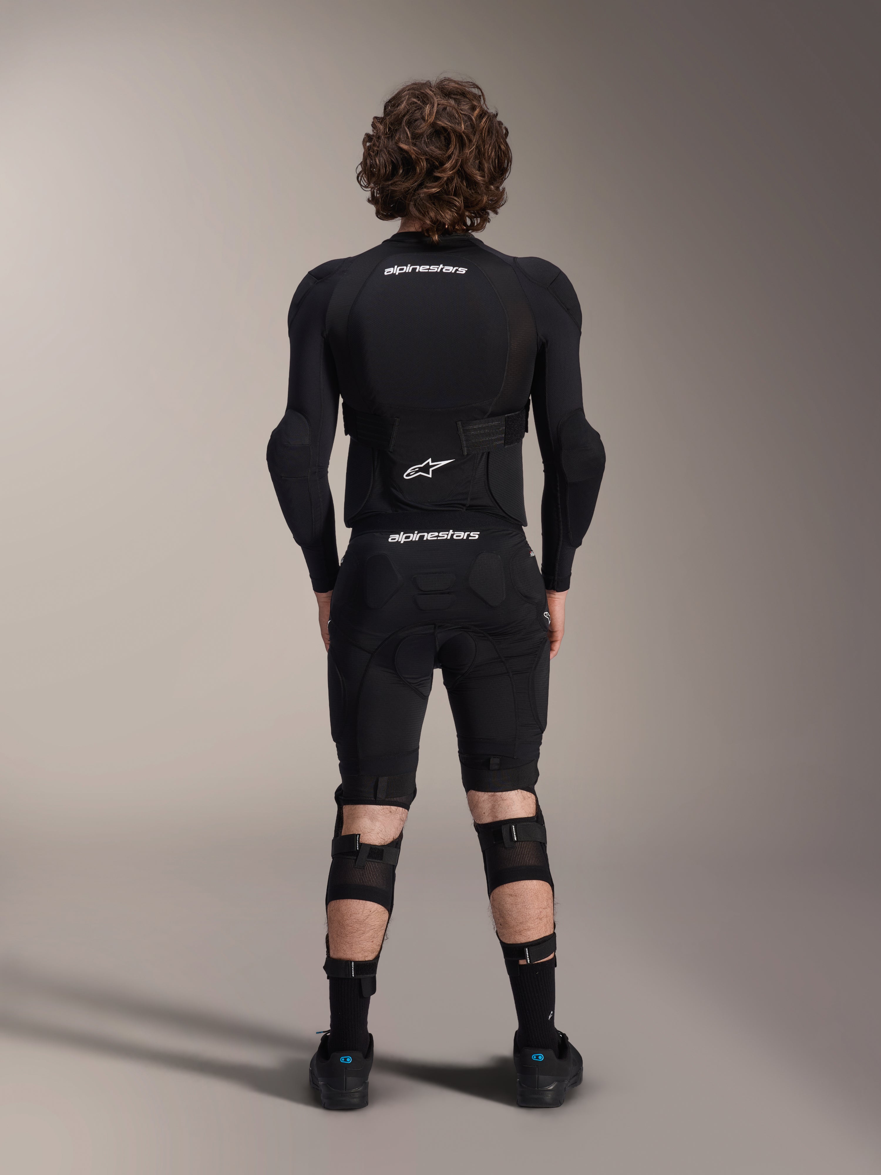 Alpinestars A-Impact Plasma Beskyttelsesjakke - Langærmet, set bagfra, sort med hvide Alpinestars-logoer, båret med beskyttelsesshorts og knæbeskyttere for fuld kropsbeskyttelse til mountainbike