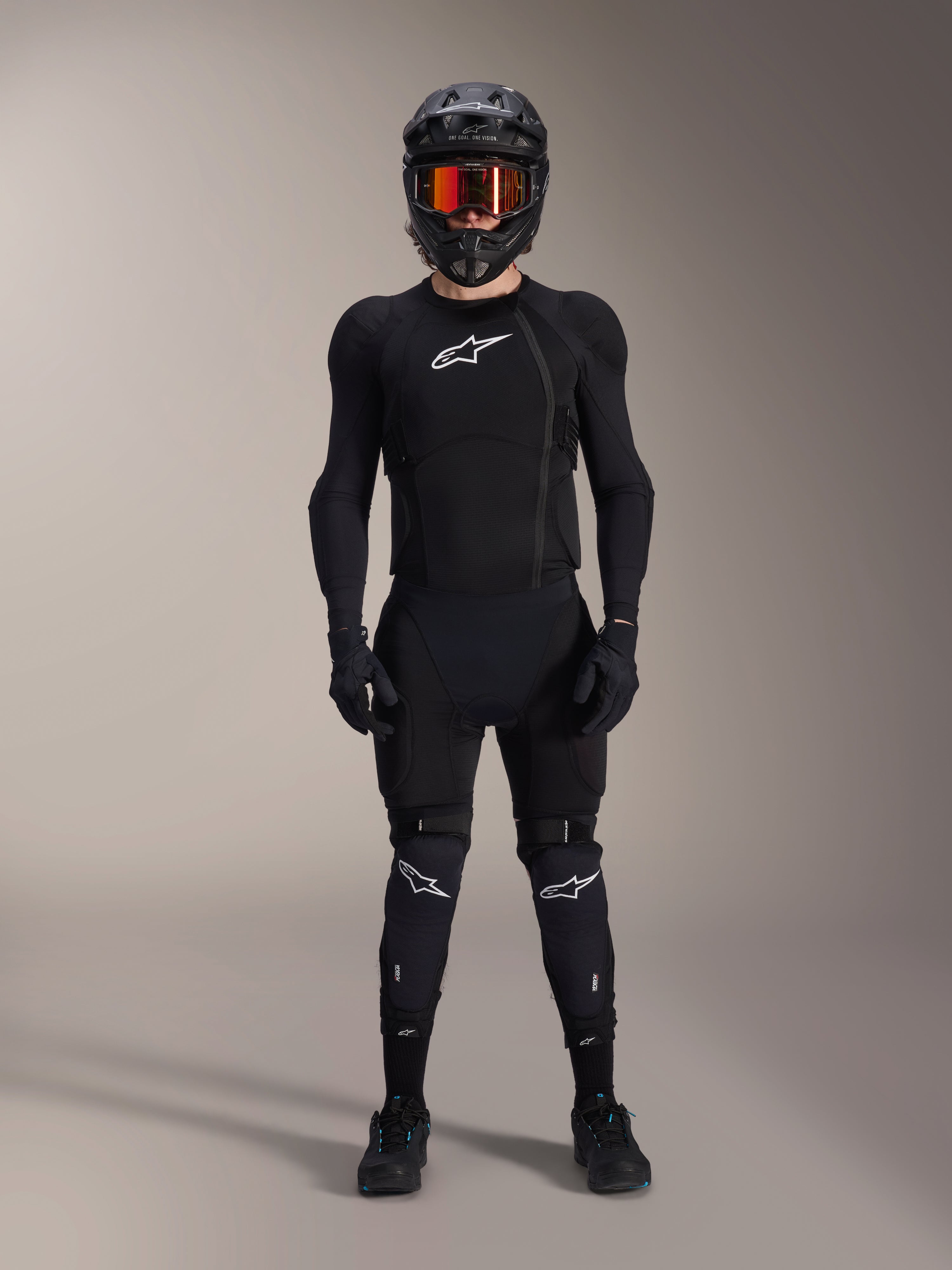 Mountainbike-rytter iført komplet beskyttelsesudstyr, Alpinestars A-Impact Plasma beskyttelsesjakke i sort og hvid, med hvidt brystlogo og mesh-stof, kombineret med sort hjelm, rødtonede goggles og knæbeskyttere, koordineret high-performance MTB-beskyttelsessæt.